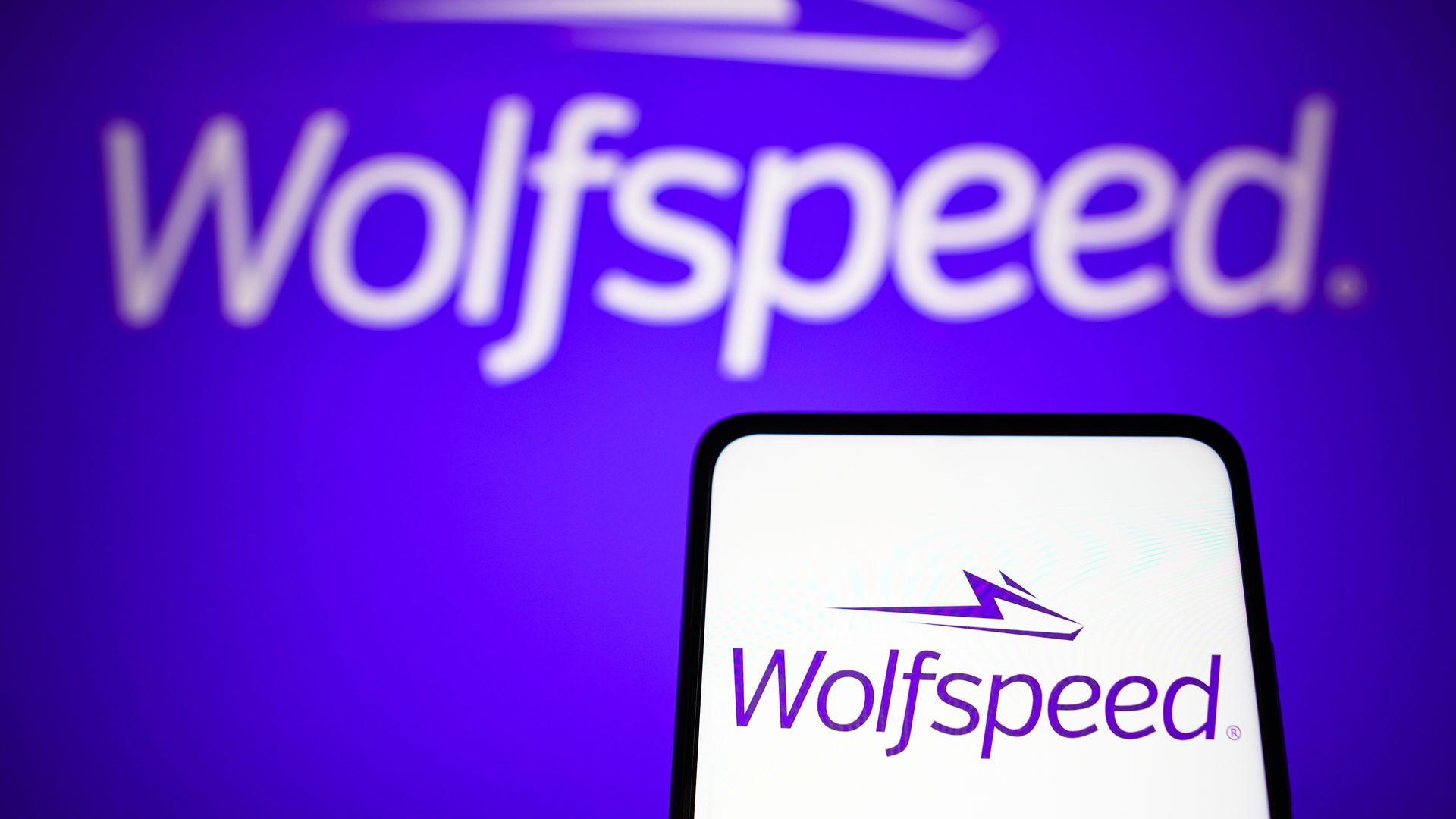 The Wolfspeed logo on a phone in front of a Wolfspeed logo on a wall.