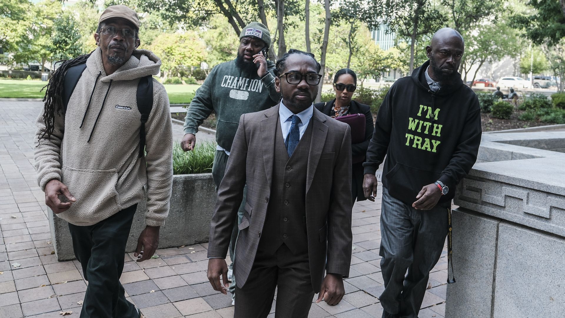 Trayon White Sr. dressed in a suit surrounded by four people. A man in a black sweatshirt to the right is printed with "I'm with Tray."