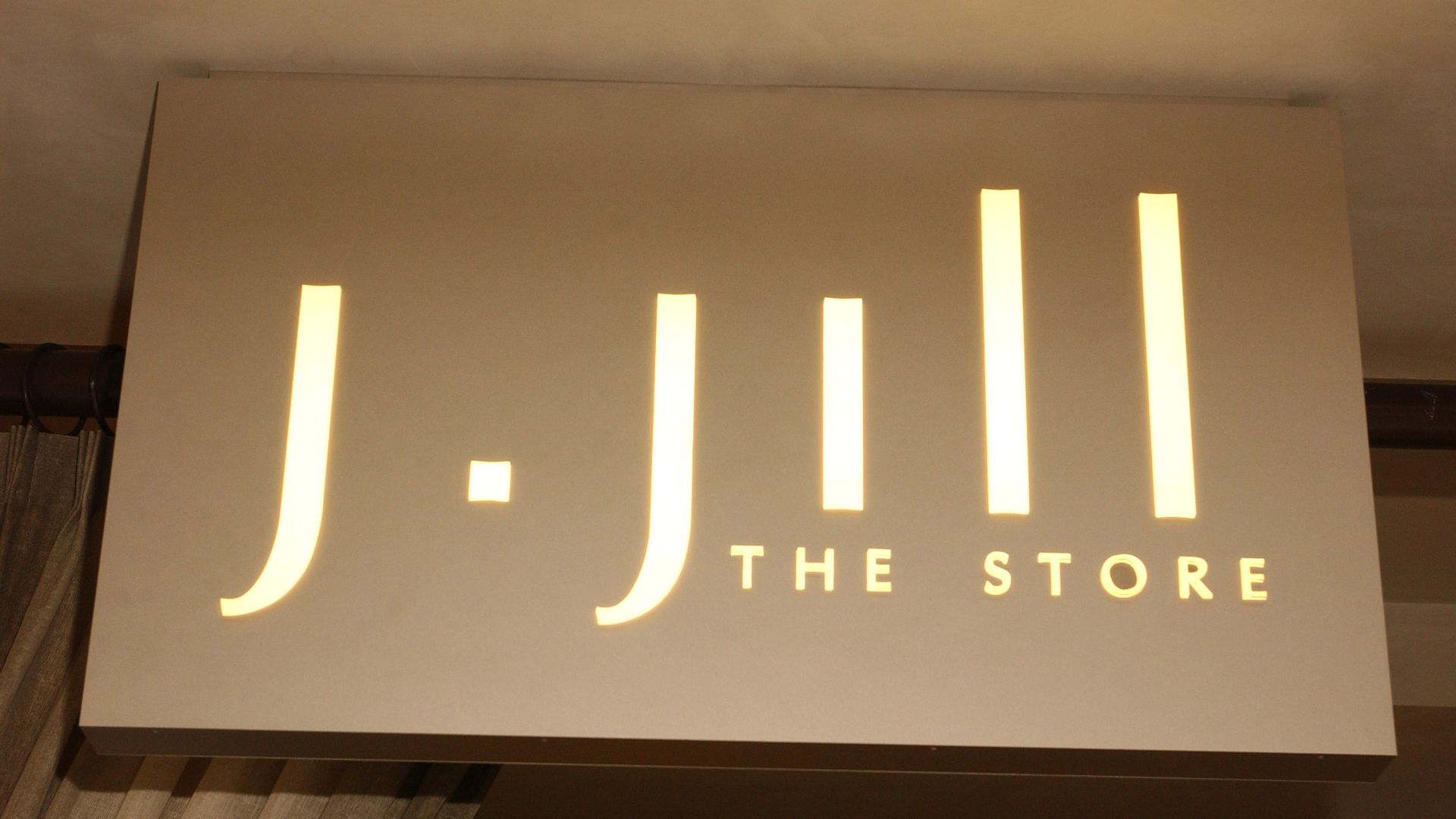 A J.Jill sign in a beige tone hangs on the wall of one of its stores.