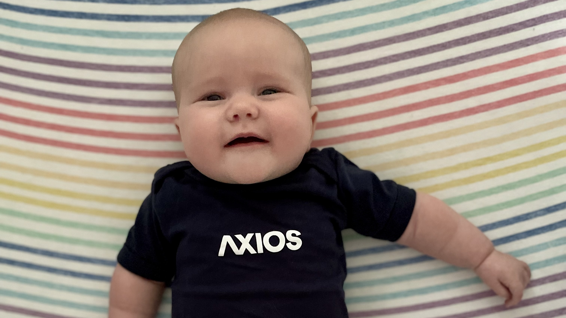 Meredith Briggs lays in her crib wearing an Axios onesie at 3 months old.