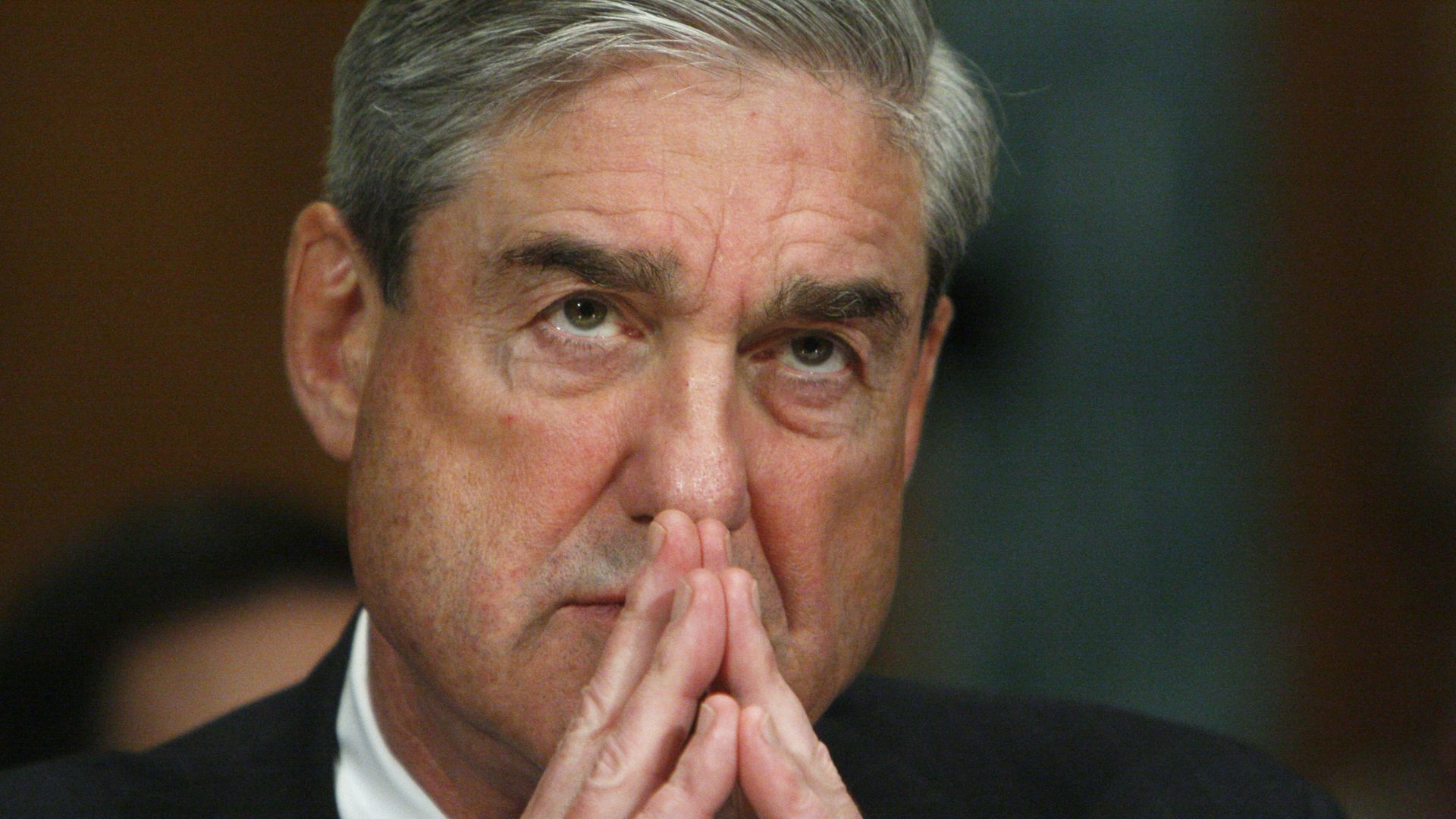 In this image, Robert Mueller listens with his fingers steepled in front of him. 