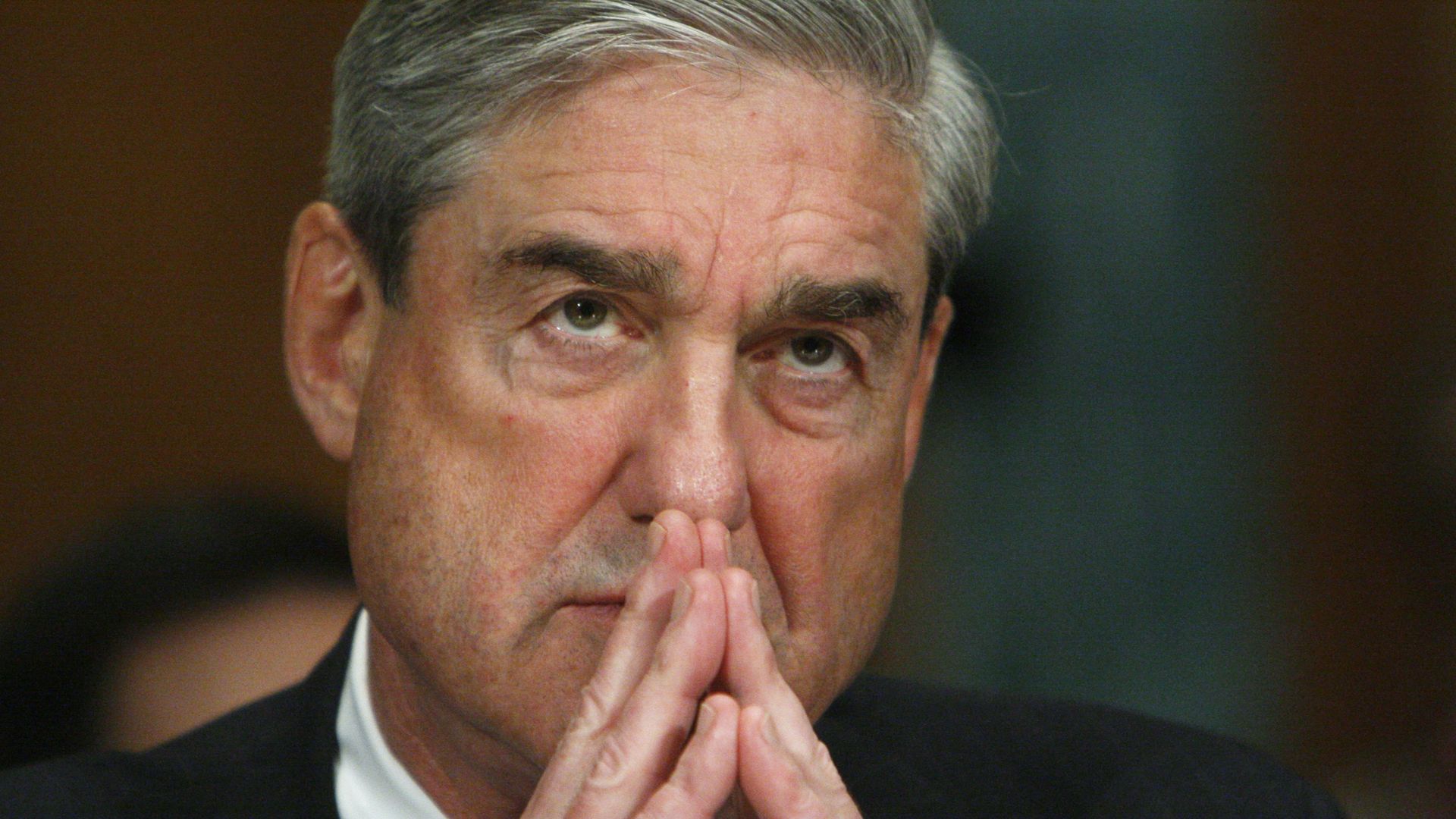 In this image, Robert Mueller listens with his fingers steepled in front of him.
