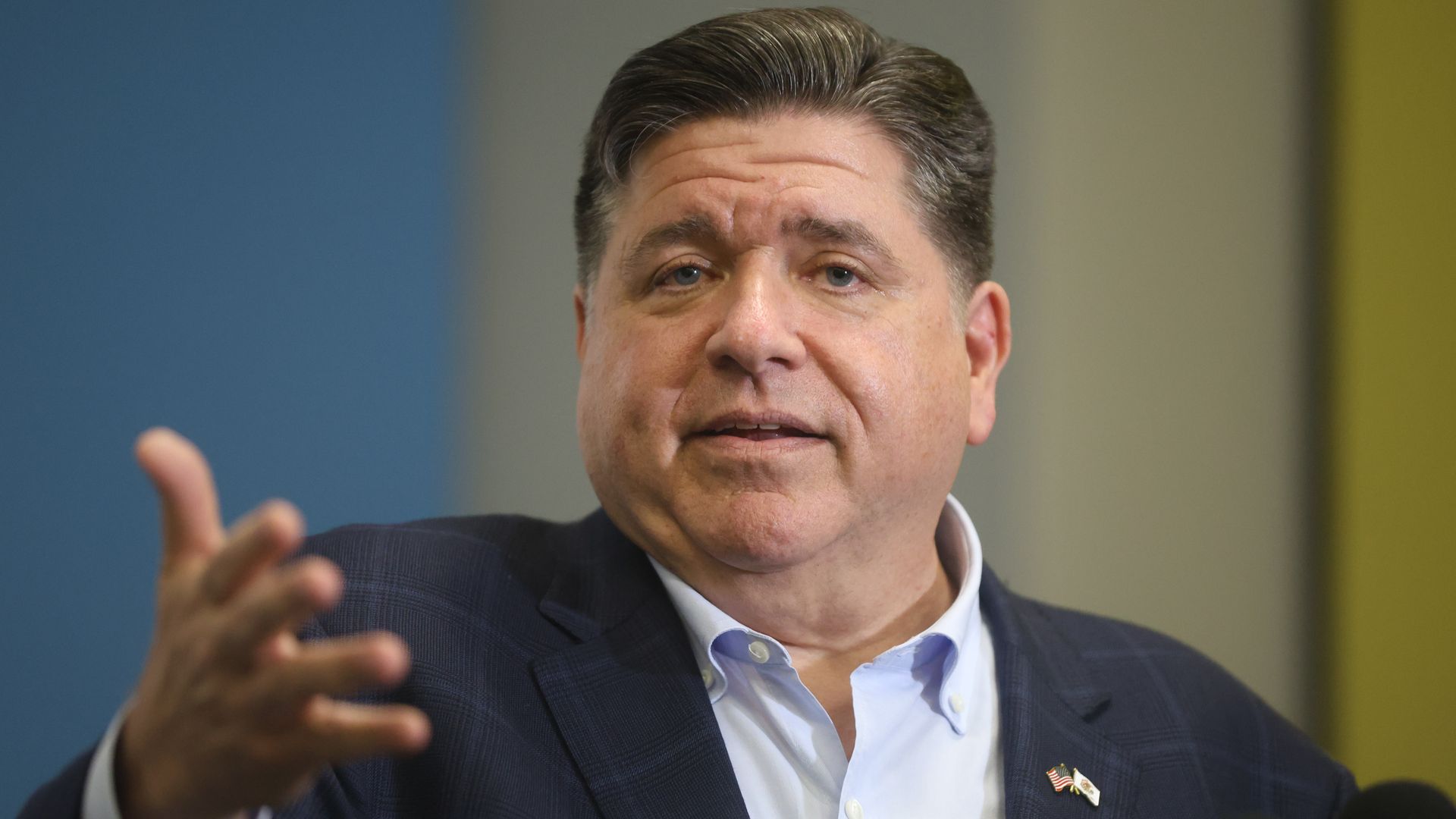 Illinois Governor JB Pritzker in navy blazer outstretching his arm toward the camera.