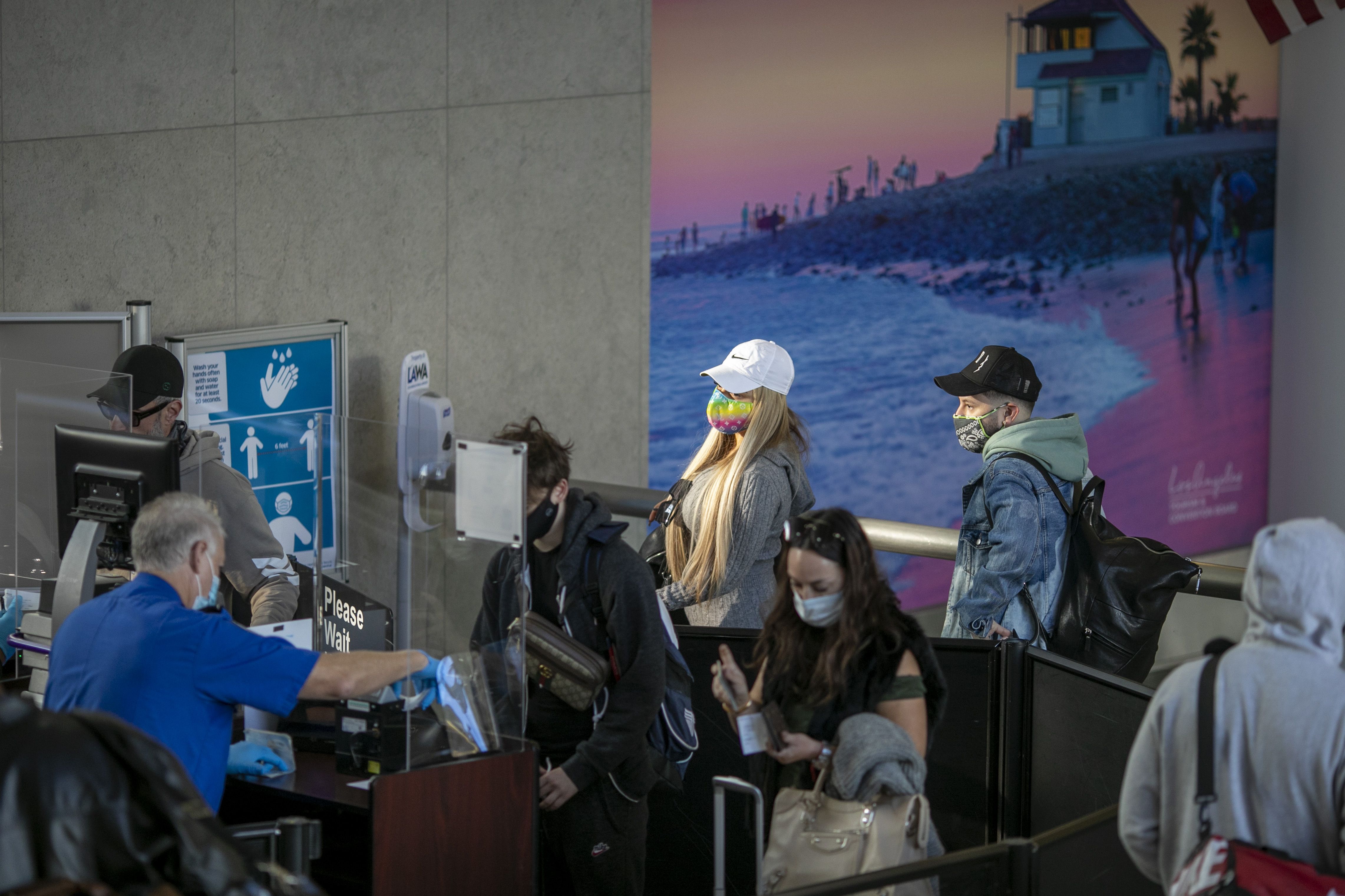 A group of people wearing face masks, three with baseball caps, stand in line while wearing face masks 