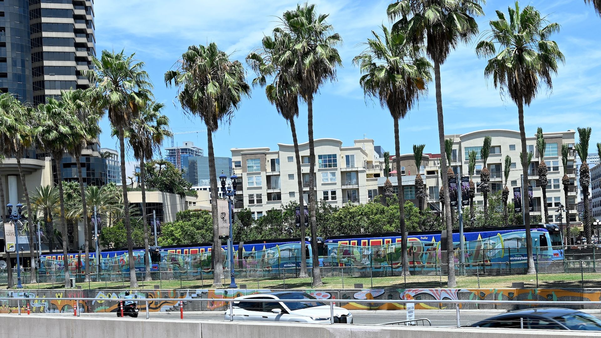 The San Diego Trolley, wrapped with blue Comic Con-themed ads, passes by condos, palm trees and cars in downtown San Diego.