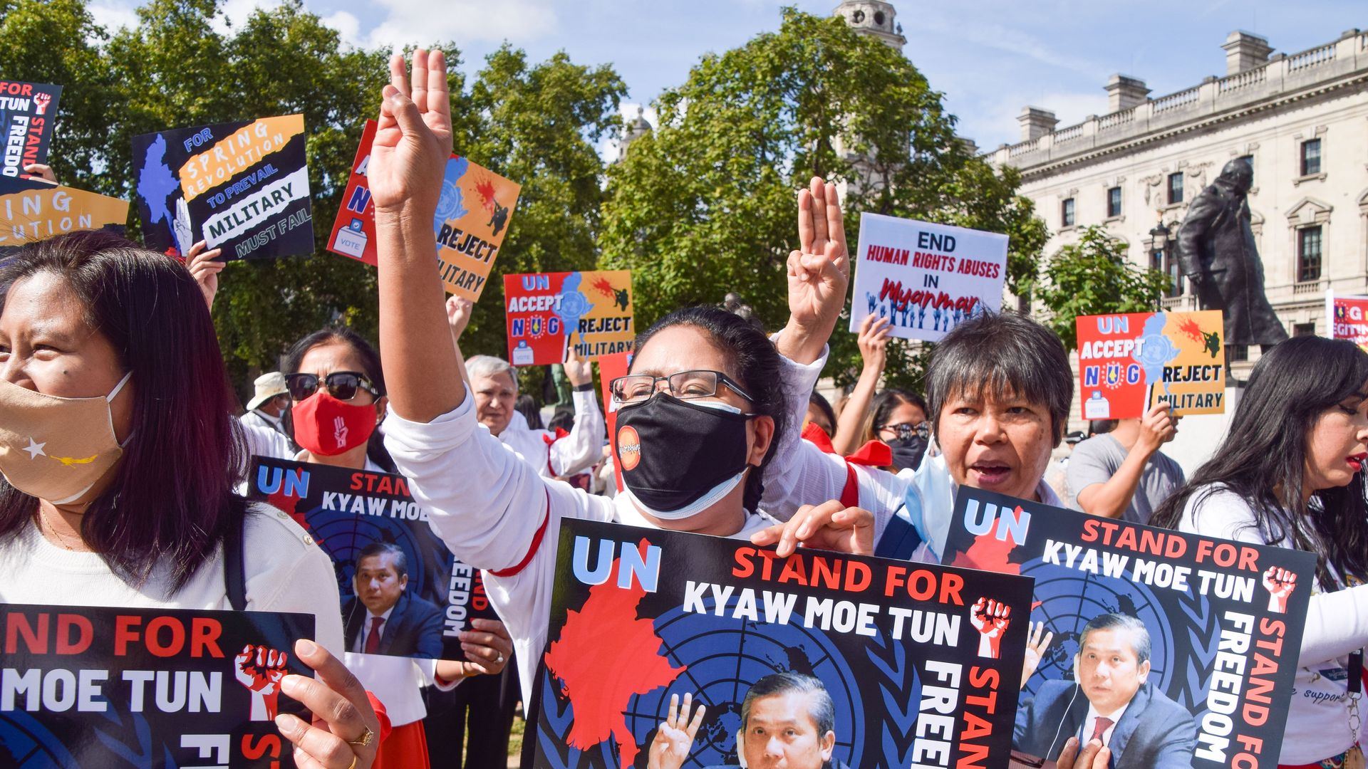 Protesters hold up the three-finger salute and placards supporting Myanmar's UN representative Kyaw Moe Tun