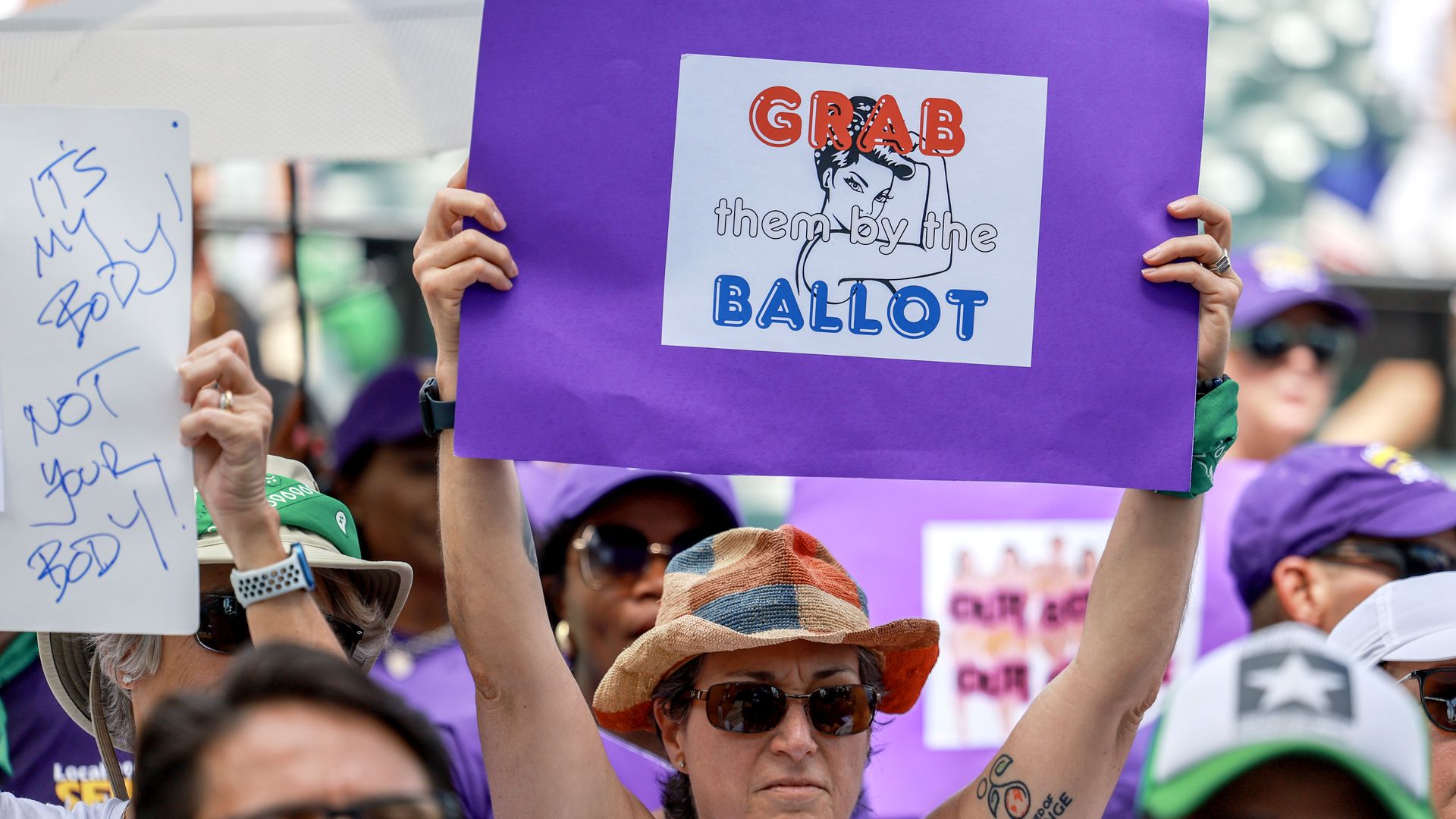 A photo shows an abortion rights demostrator holding a sign that says "grab them by the ballot."
