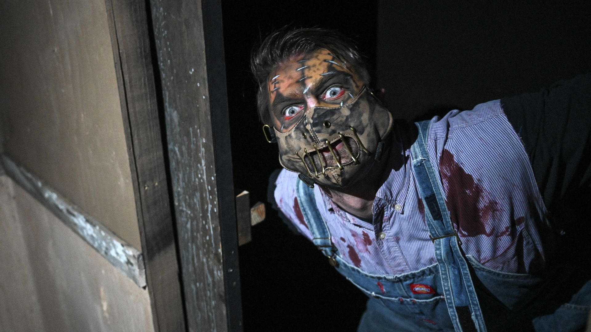 An actor in a mask covered in blood pops out at Field of Screams