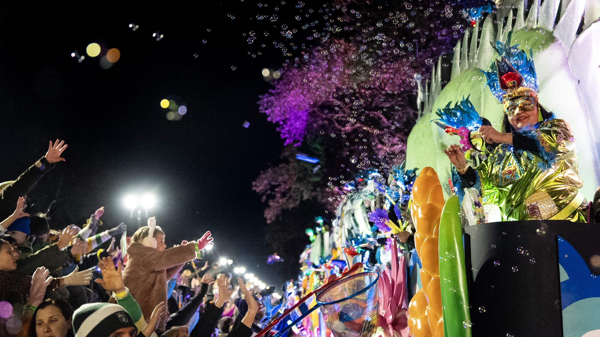 A Mardi Gras float rolls past a crowd during a nighttime parade.
