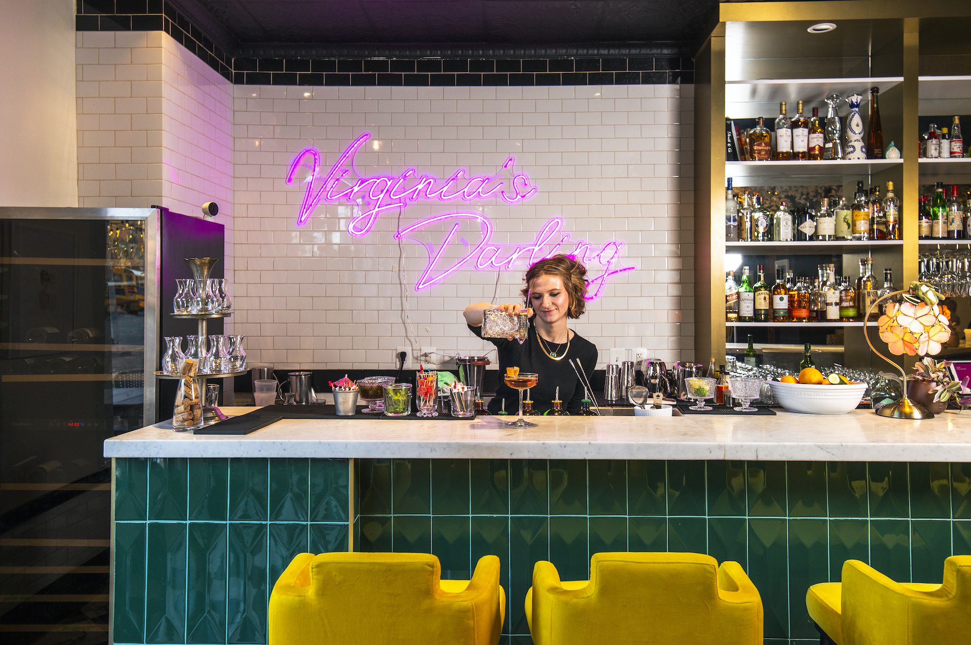 A woman in a black t-shirt pours a cocktail behind the bar at Virginia's Darling