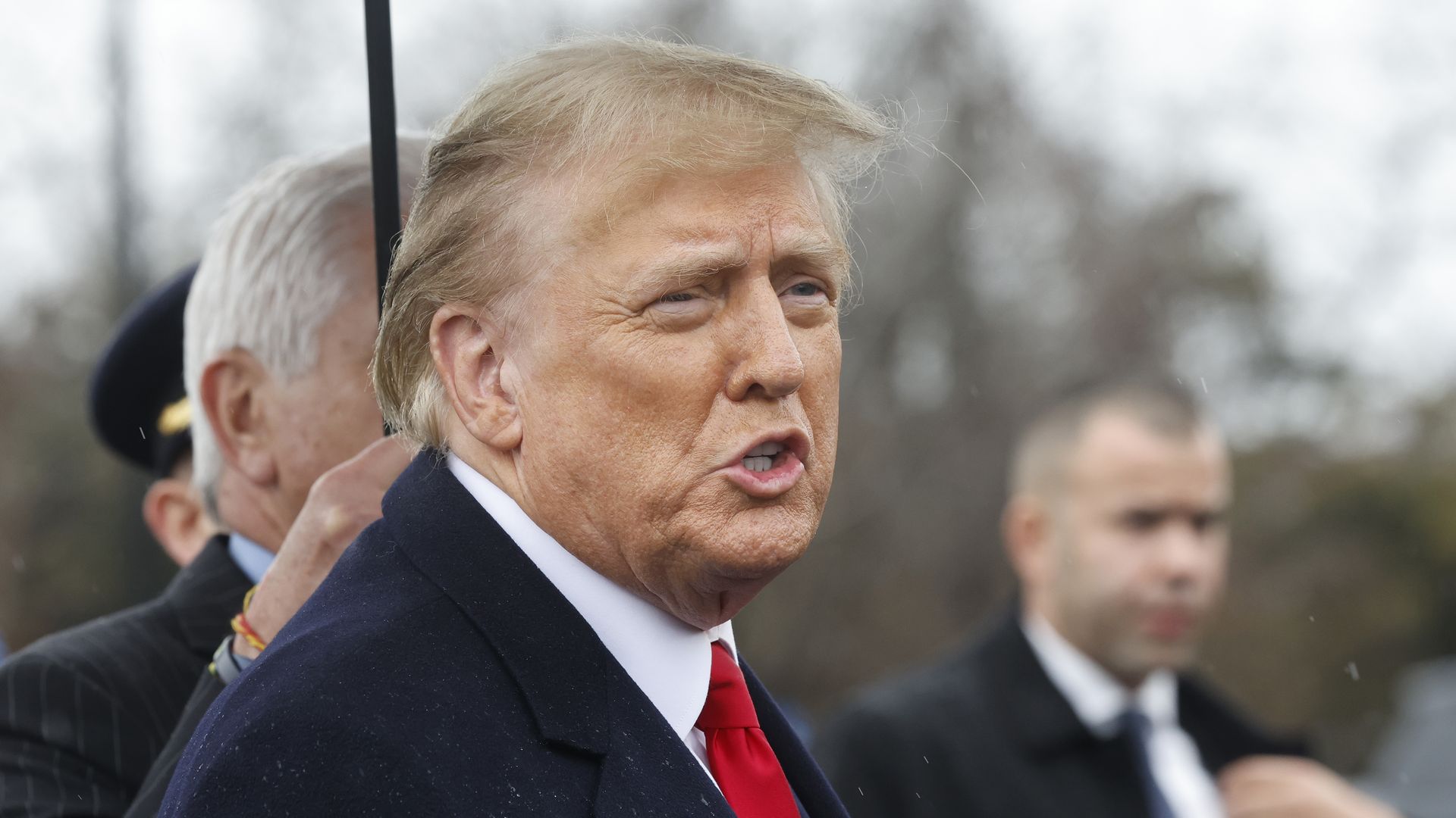 Former President Donald Trump speaks while someone holds an umbrella over him.