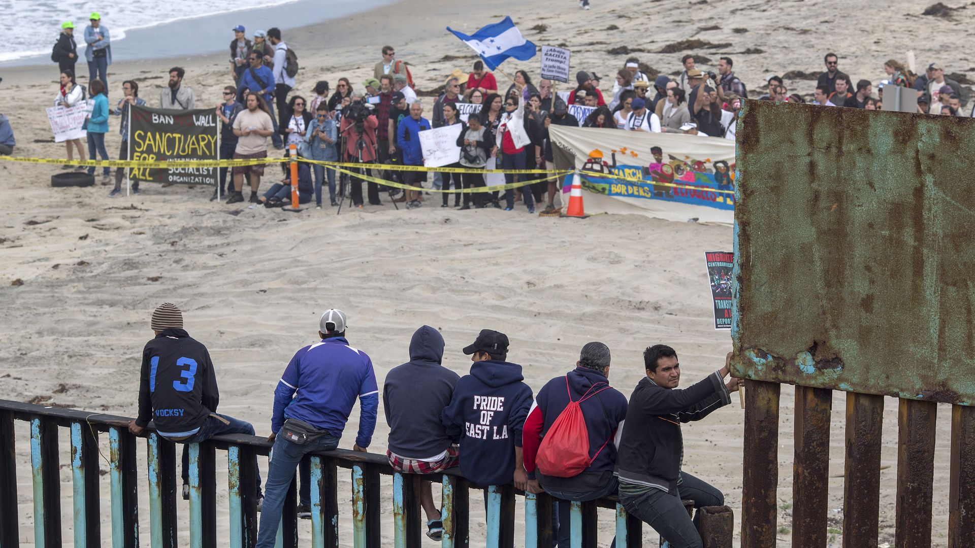 People climb a section of border fence to look toward supporters in the U.S. as members of a caravan of Central American asylum seekers 