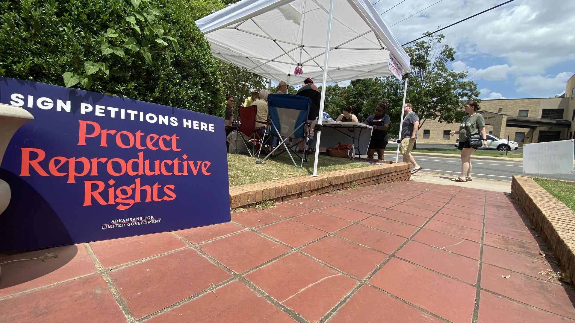 A woman approached a tent where people are signing petitions and in the foreground is a sign reading: Protect Reproductive Rights.