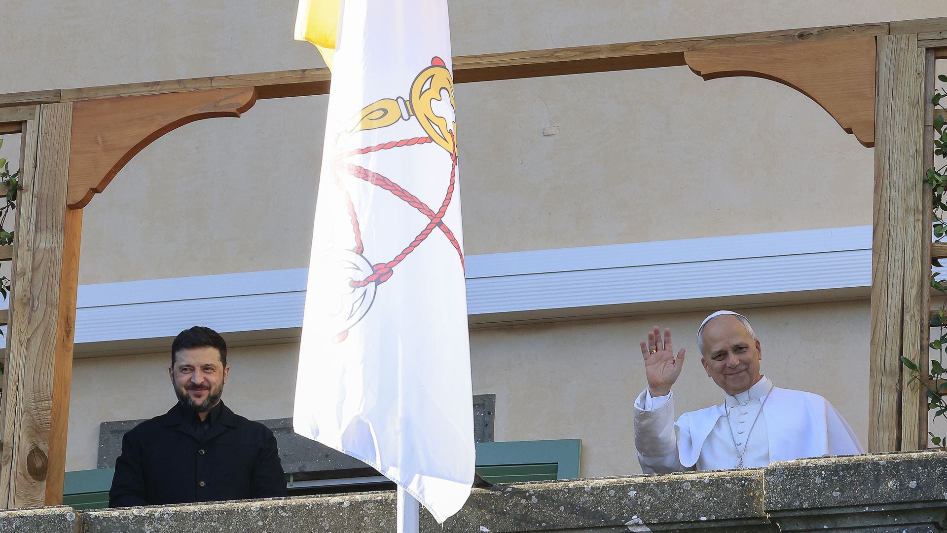 Volodymyr Zelensky and Pope Leo stand on a balcony together while Pope Leo waves.