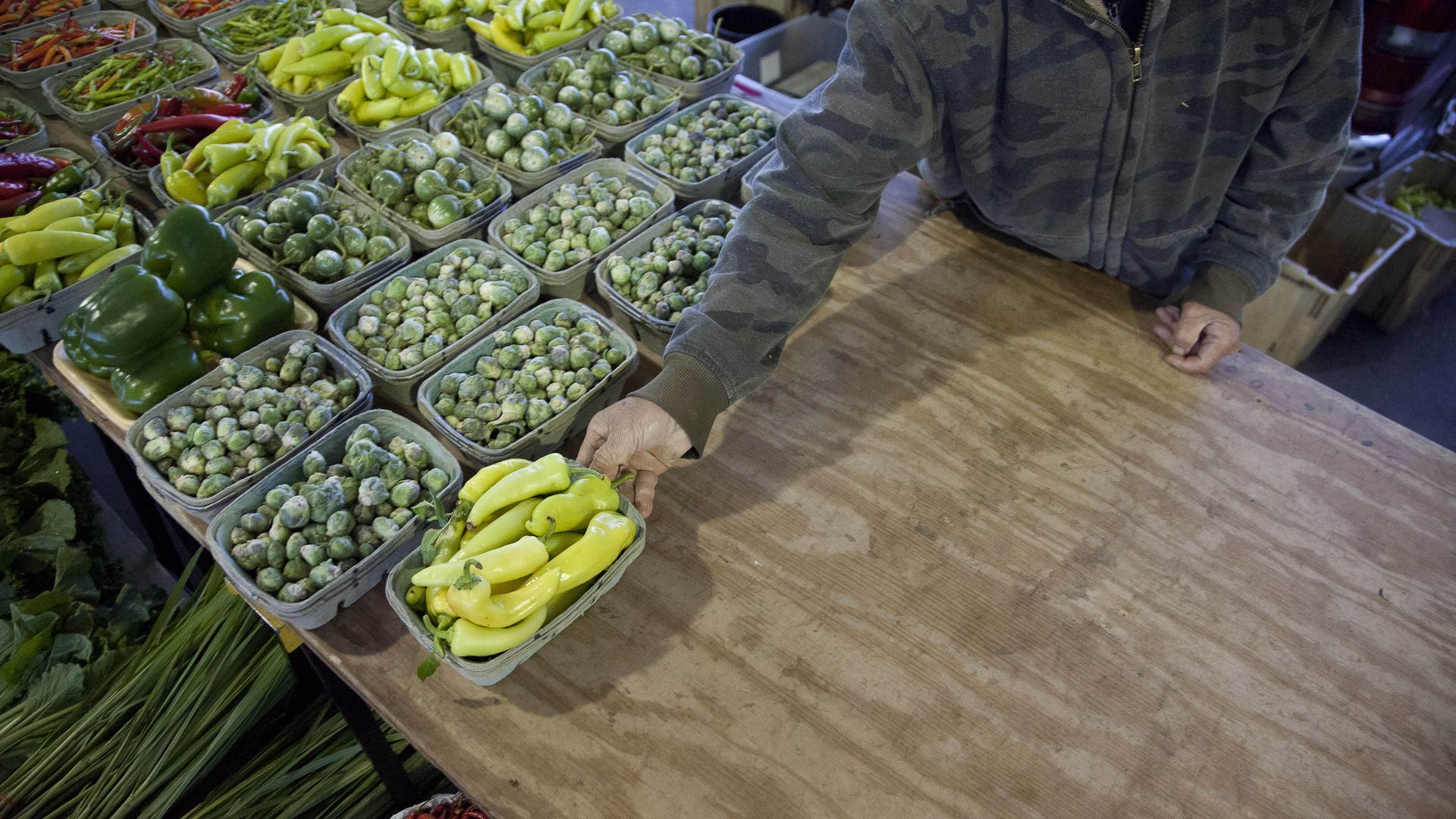 A person setting out produce onto a wooden table at a farmer's market.