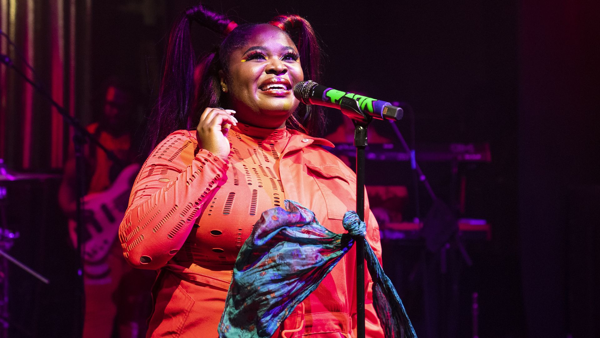 Tarriona "Tank" Ball performs at a microphone wearing pigtails and a red long-sleeved top.