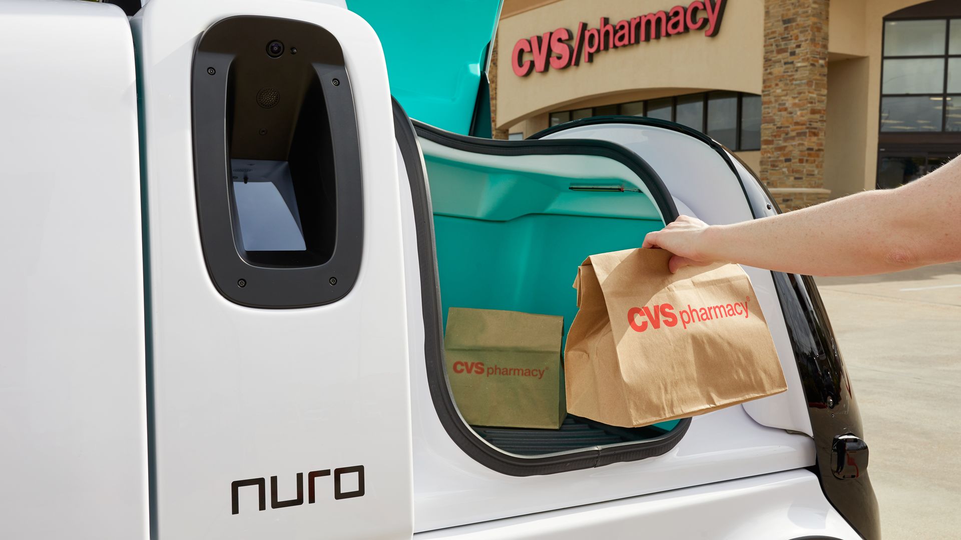 Image of person placing a CVS bag into one of Nuro's self-driving delivery vehicles. 