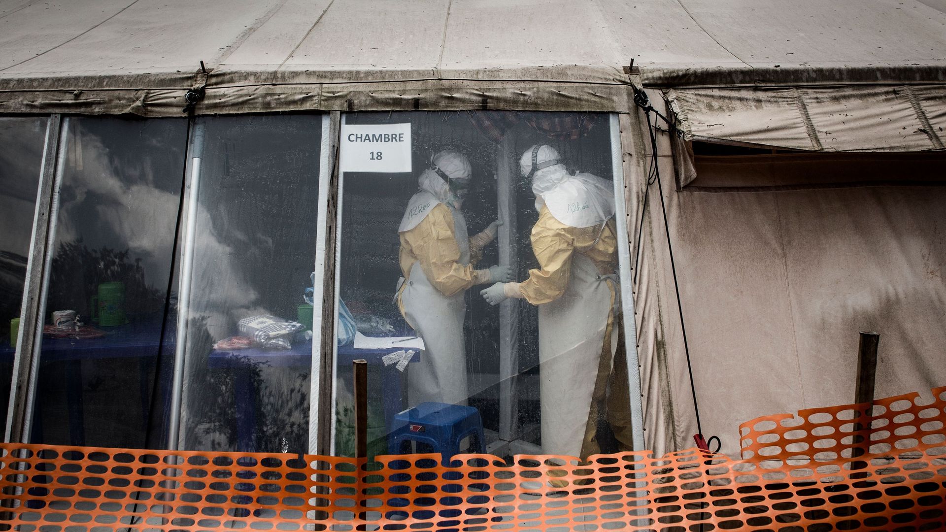 Health workers in hazmat suits are seen inside the 'red zone' of an Ebola treatment centre, behind an orange barrier. 