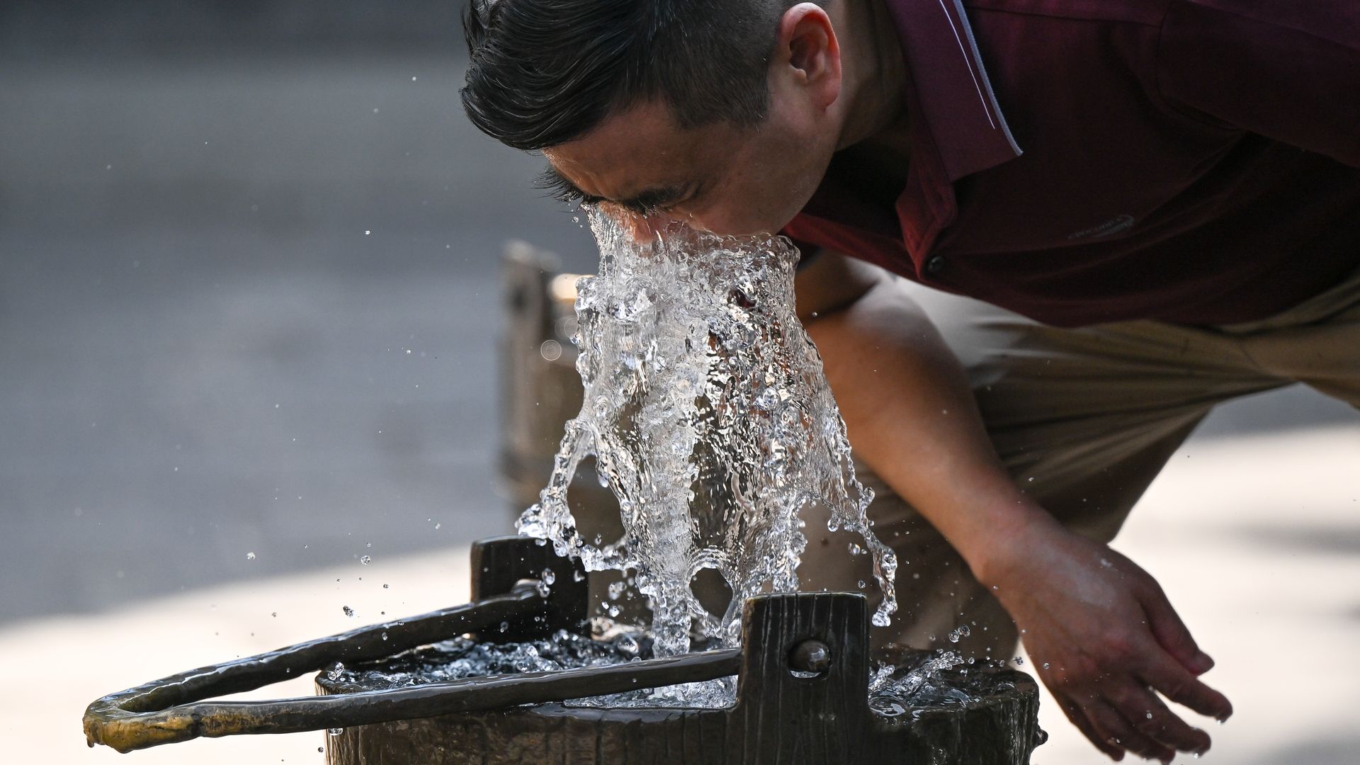 A man leans over a water fountain during a heat wave.