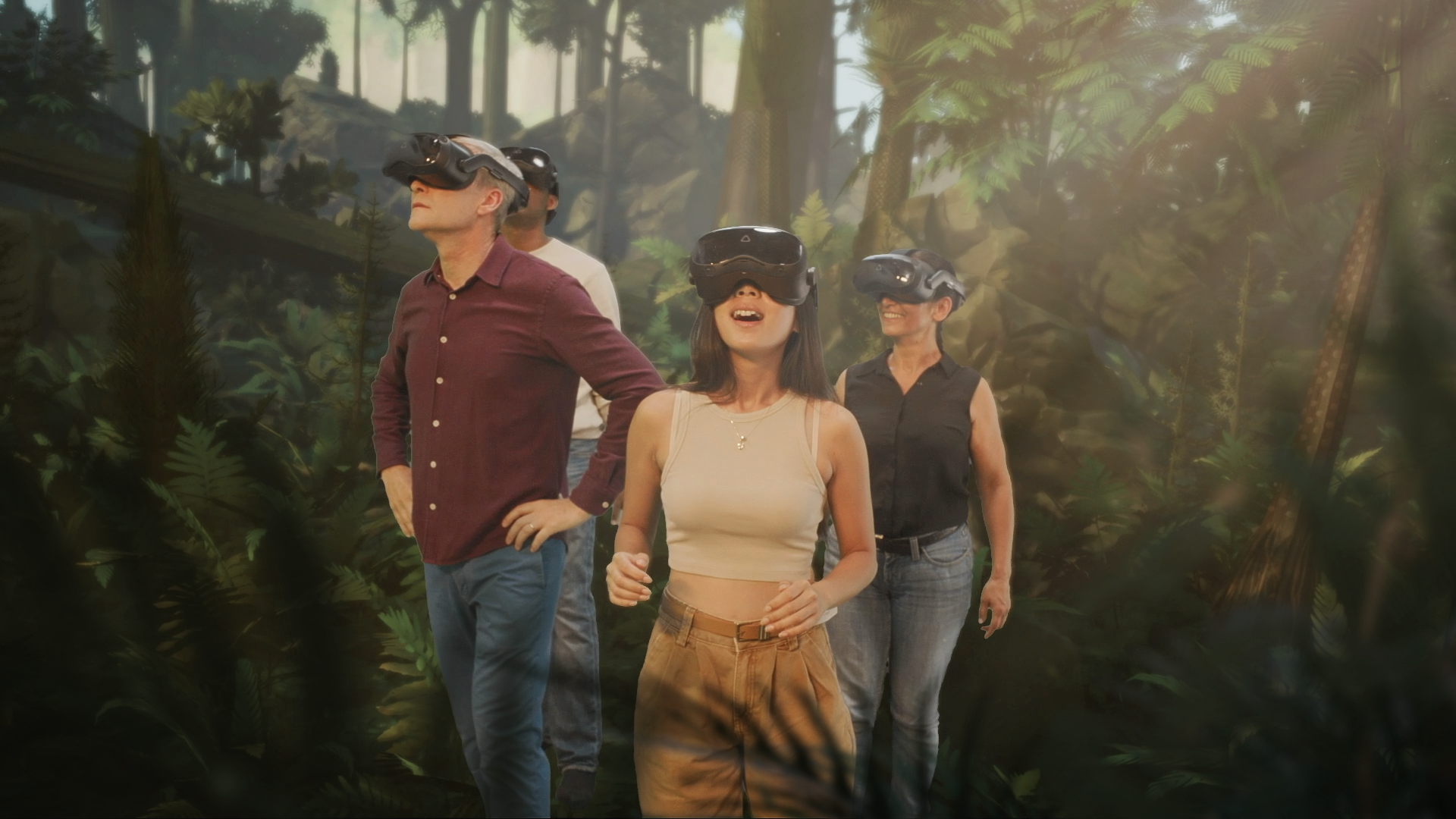 Four adults wearing VR headsets walk through a lush, sunlit forest exhibit with ferns and tall trees, looking upward with smiles.