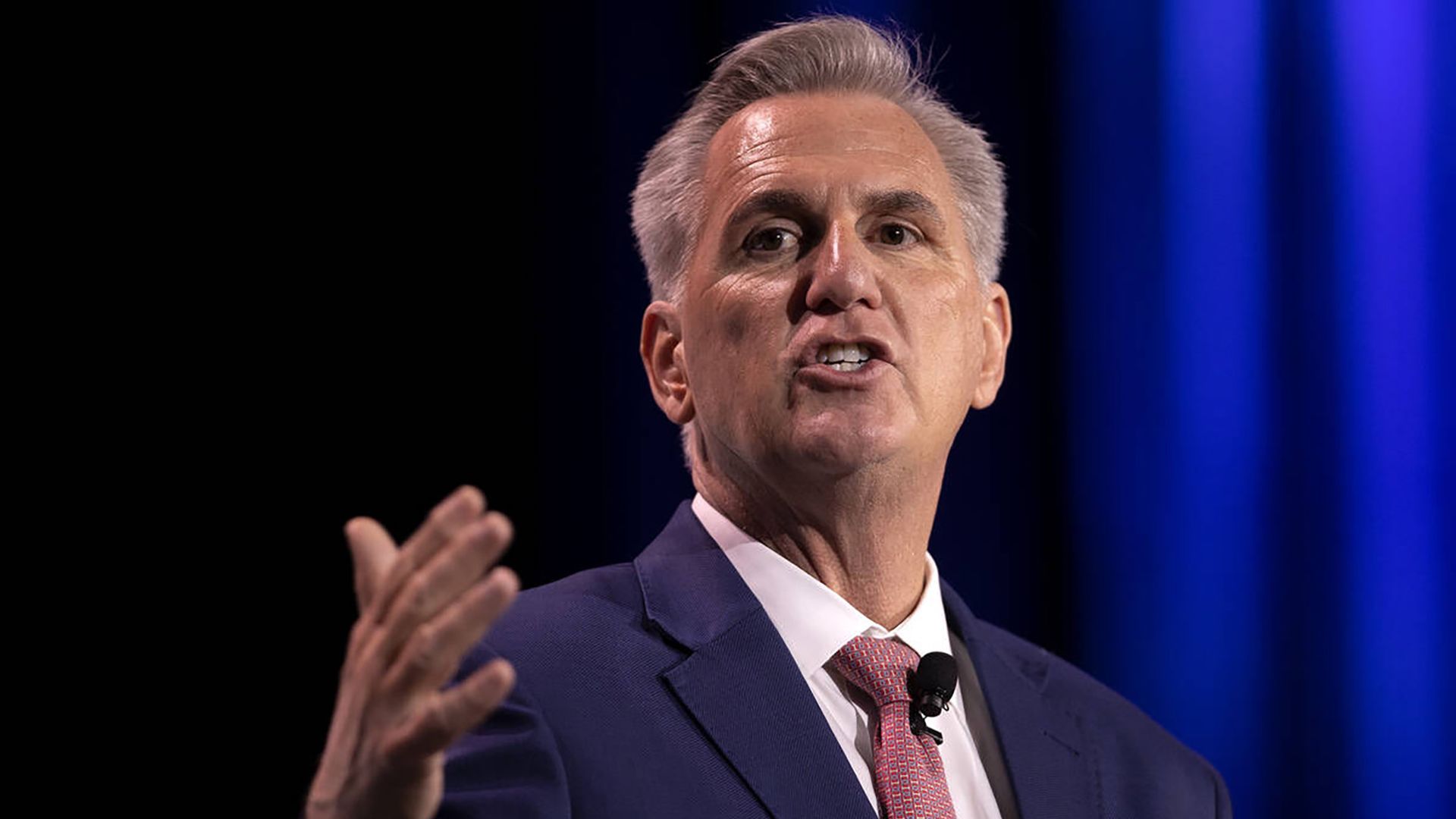 House Minority Leader Kevin McCarthy wearing a blue suit jacket, white shirt and red tie, speaks in front of a blue backdrop at the Republican Jewish Coalition leadership meeting in Las Vegas. 