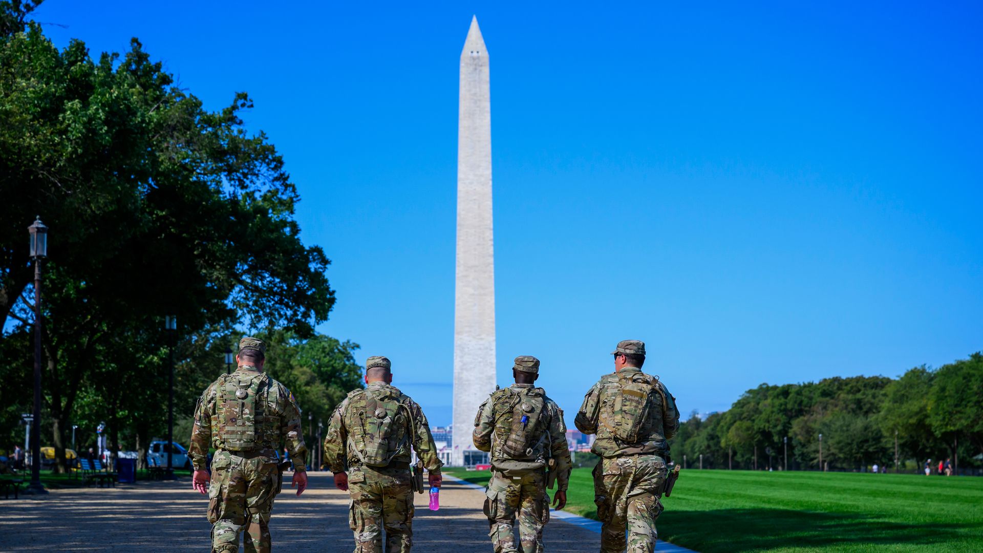Four National Guard members in their uniforms walk along the National Mall in D.C. toward the Washington Monument.