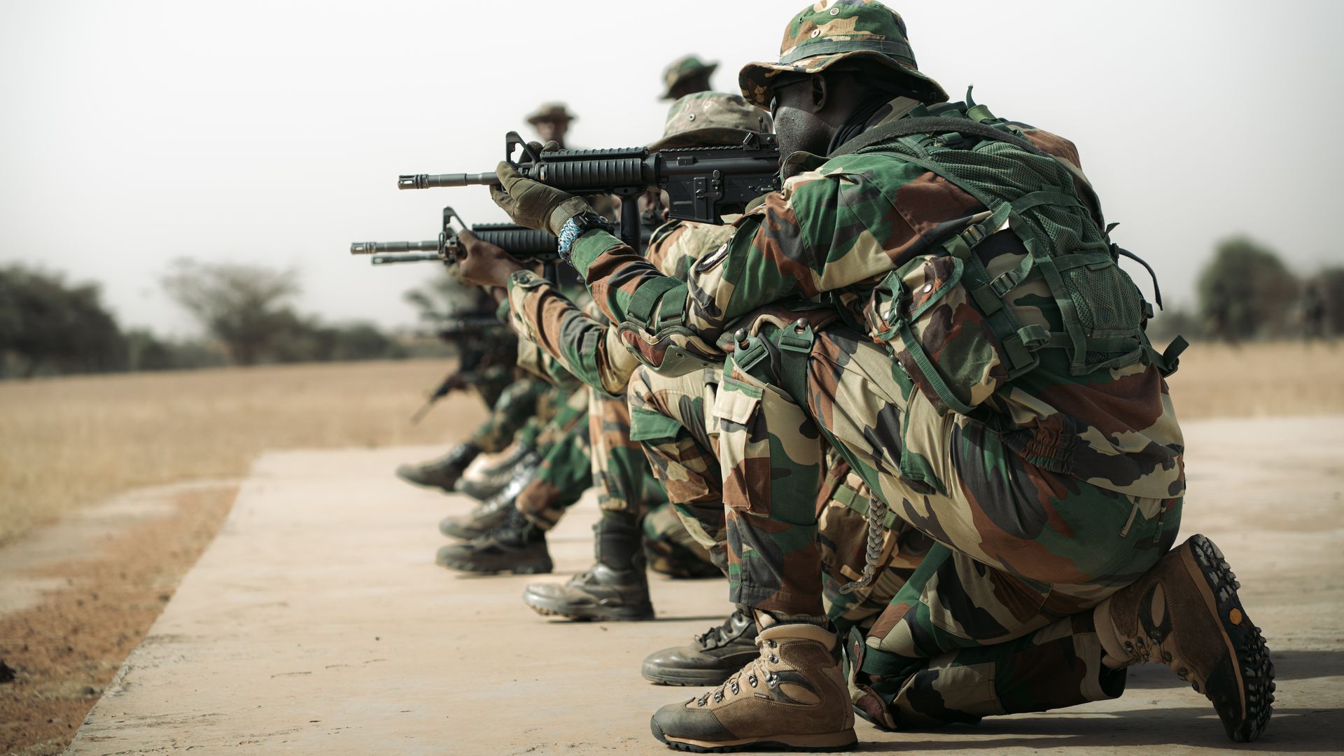 Men in military uniform are crouch in a line, staring down their gun sights.