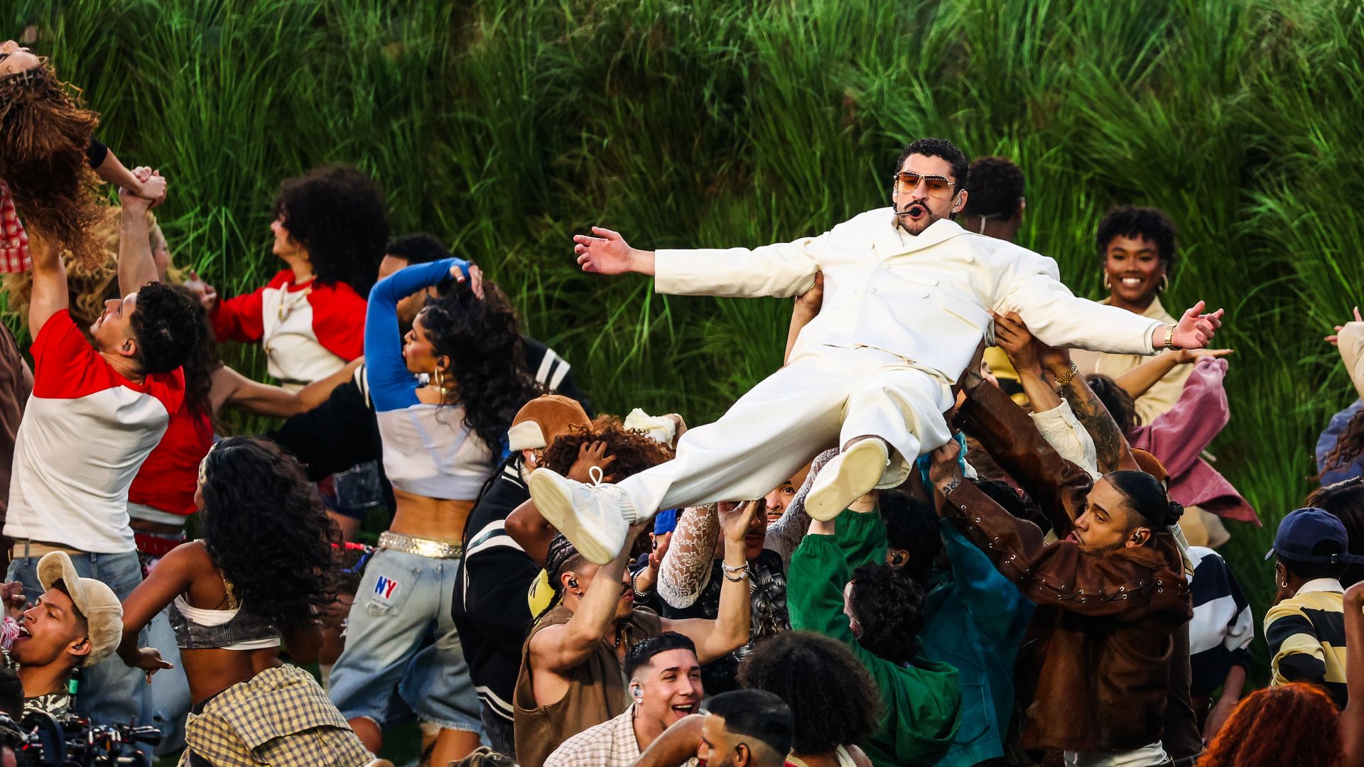 a man in a white suit falling onto a crowd of people who are holding up. Others dance around him