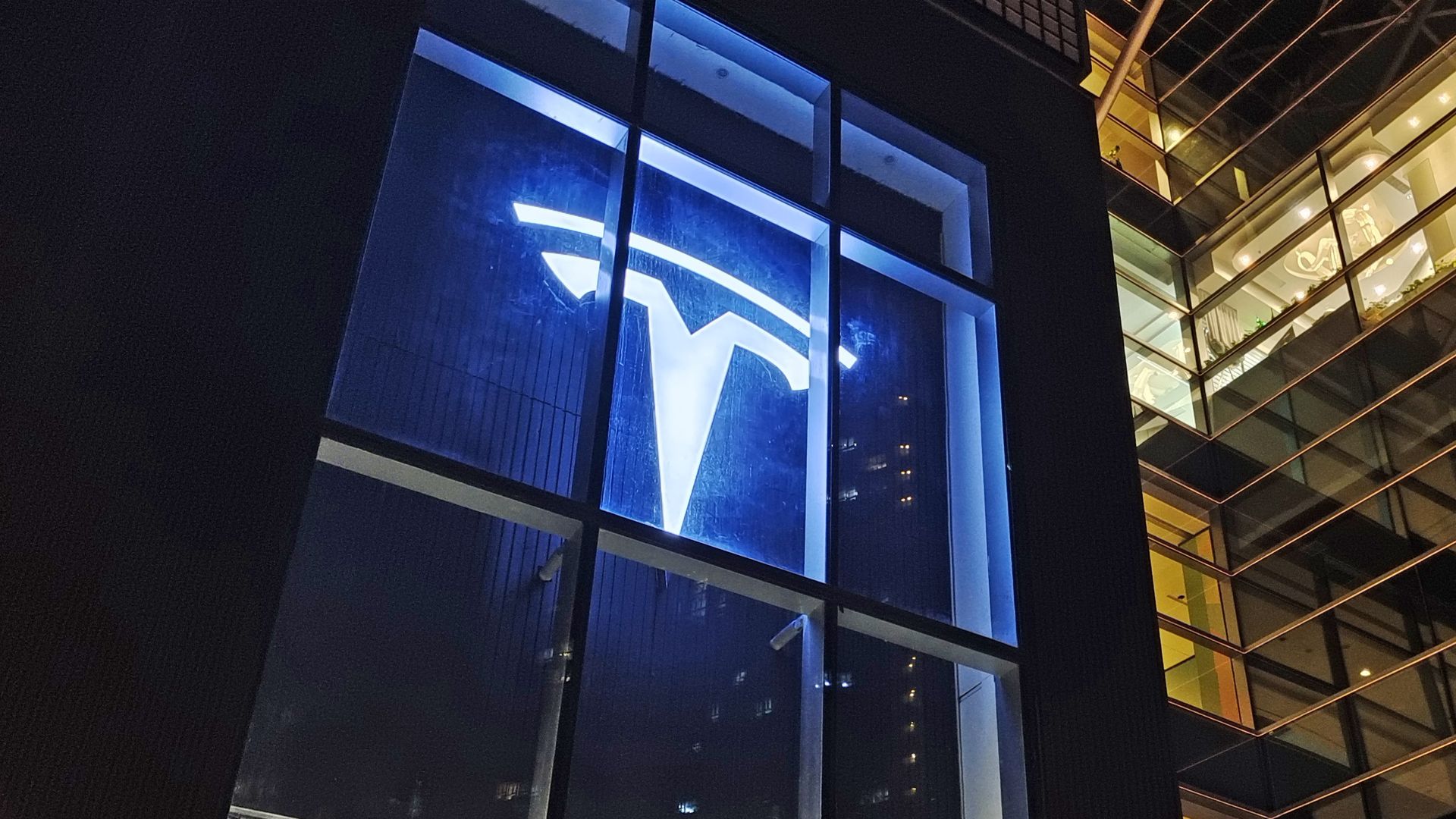 The Tesla logo glows blue in the window of a showroom in Shanghai at night.