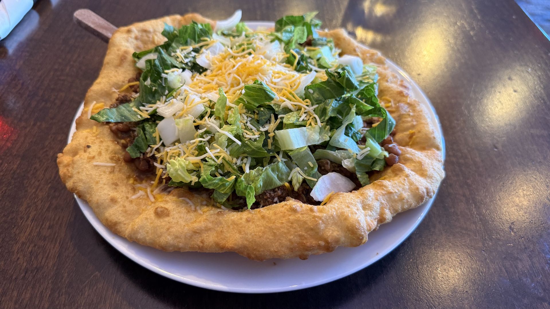 A large, round piece of frybread topped with ground bison, lettuce, onions and cheese. 