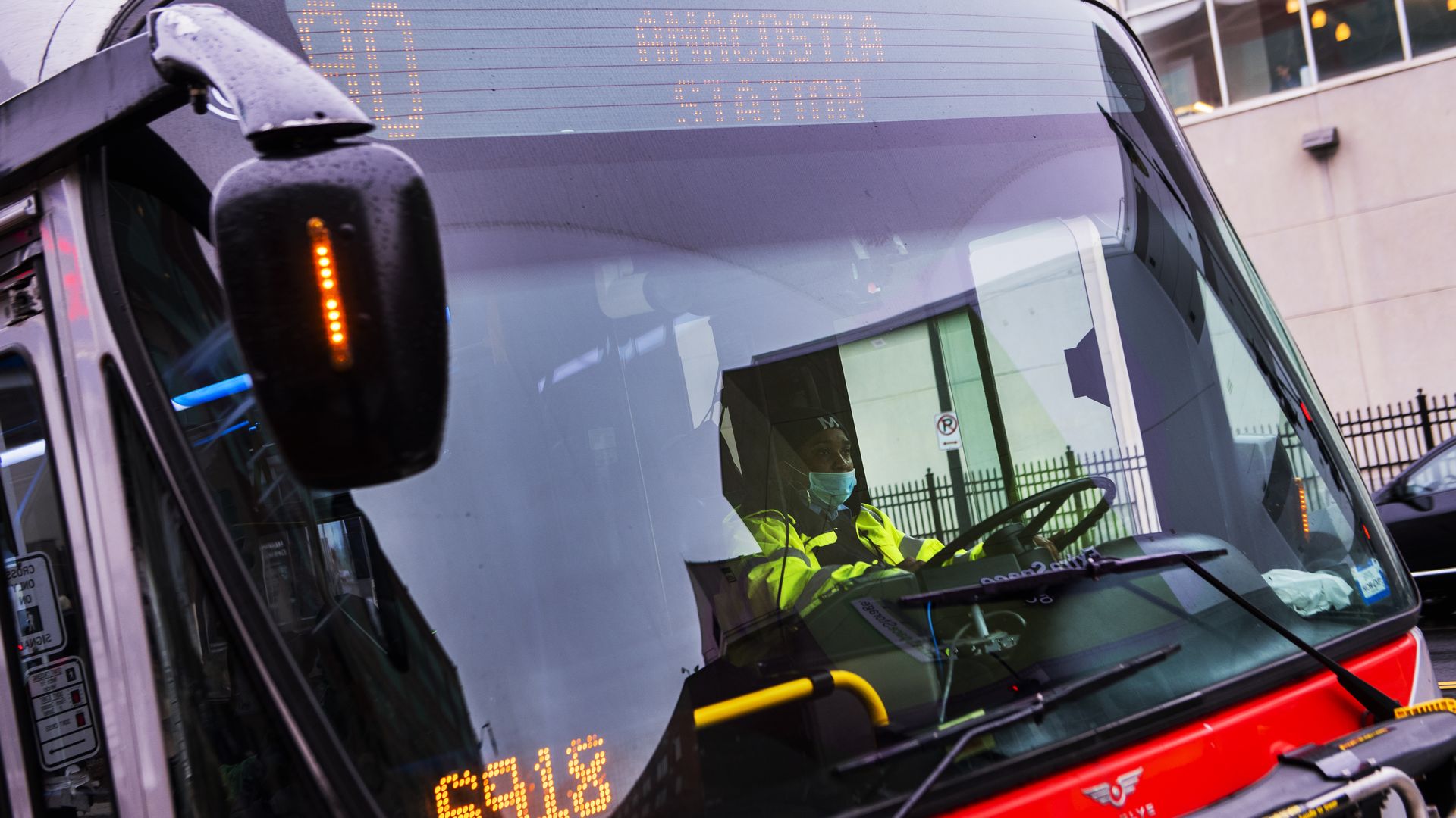 A close-up of the D.C. metrobus with a bus driver in a yellow jacket, wearing a blue face mask. 