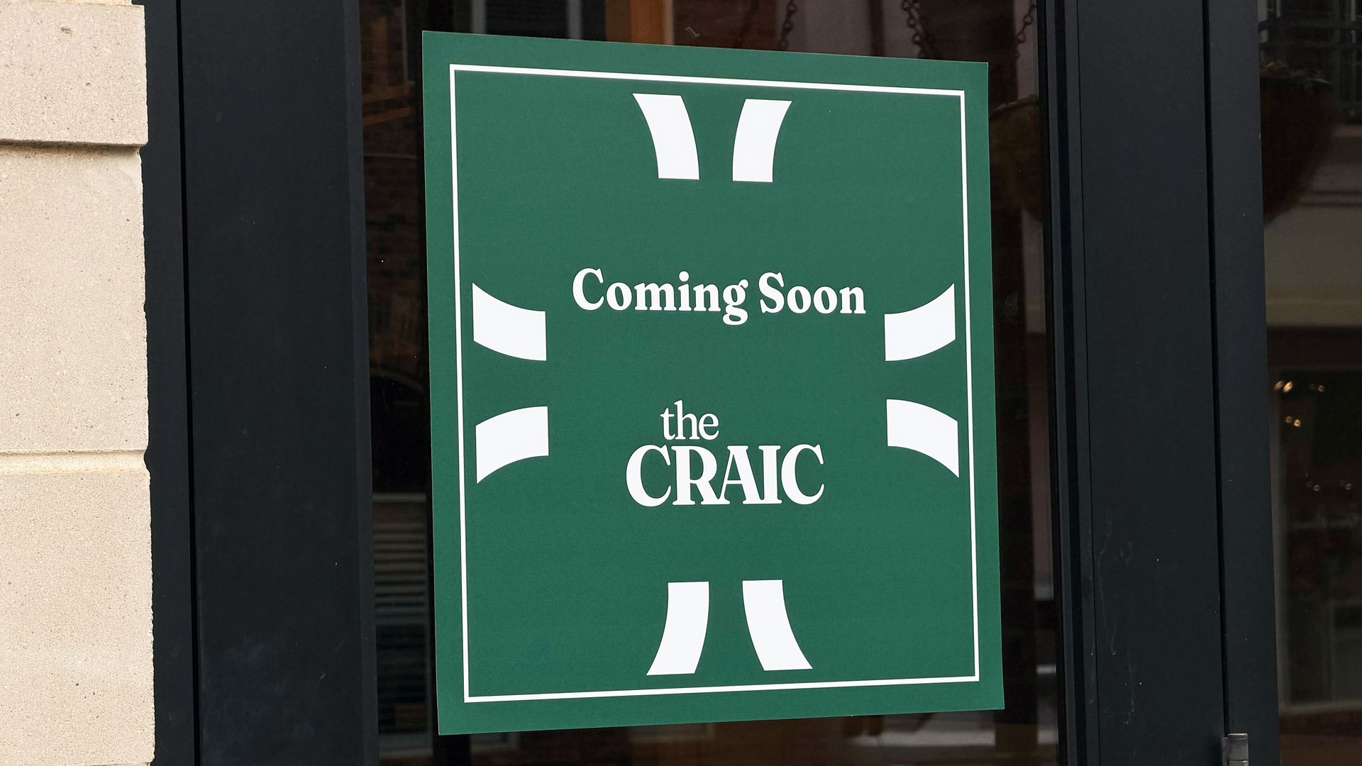 Green sign on a glass door reads "Coming Soon the CRAIC" with white markings, above a smaller sign directing to "PLEASE USE FRONT DOOR" with an arrow pointing left.