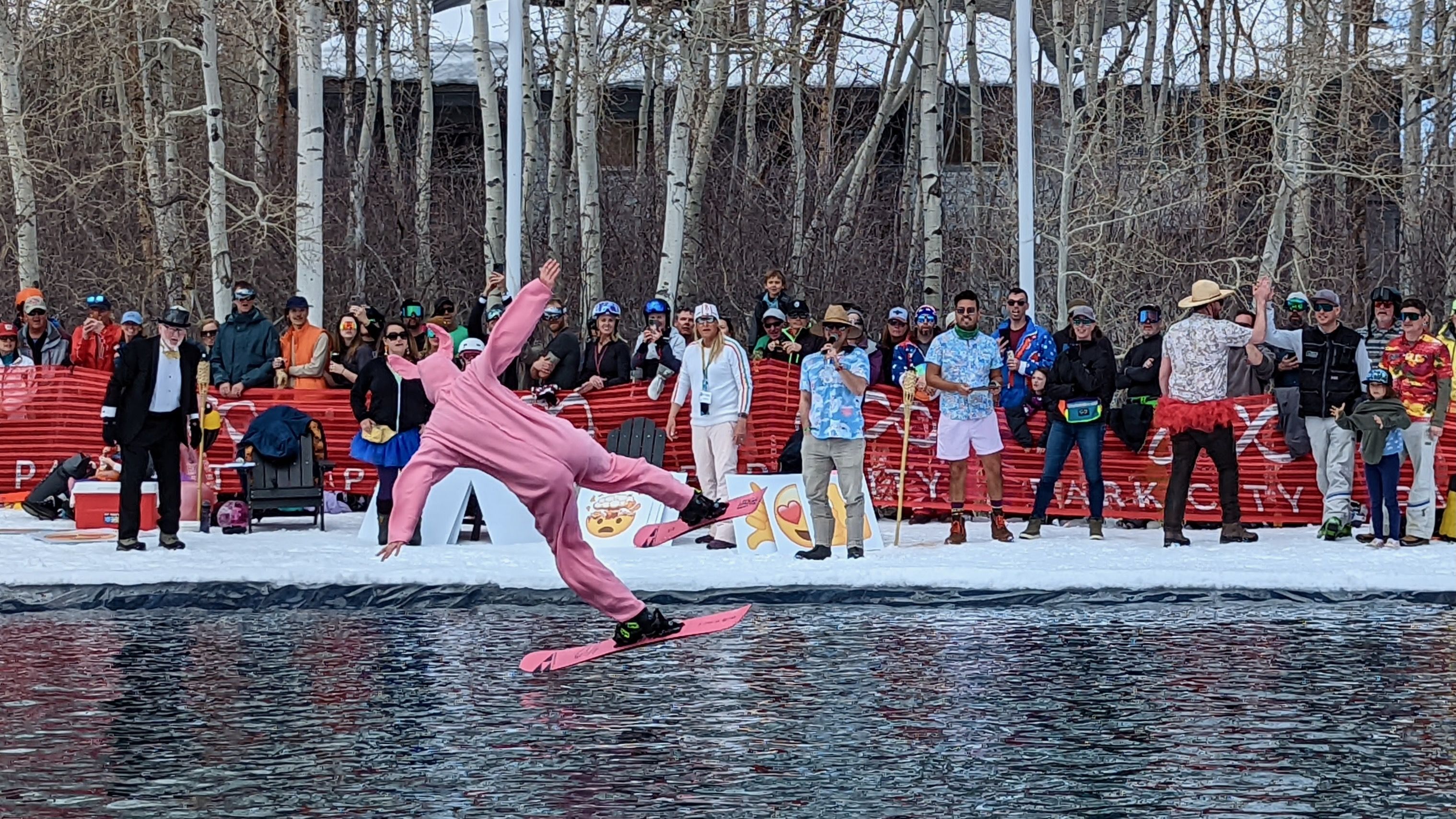 A skier dressed as a pink bunny flies over a pond after a ski jump.