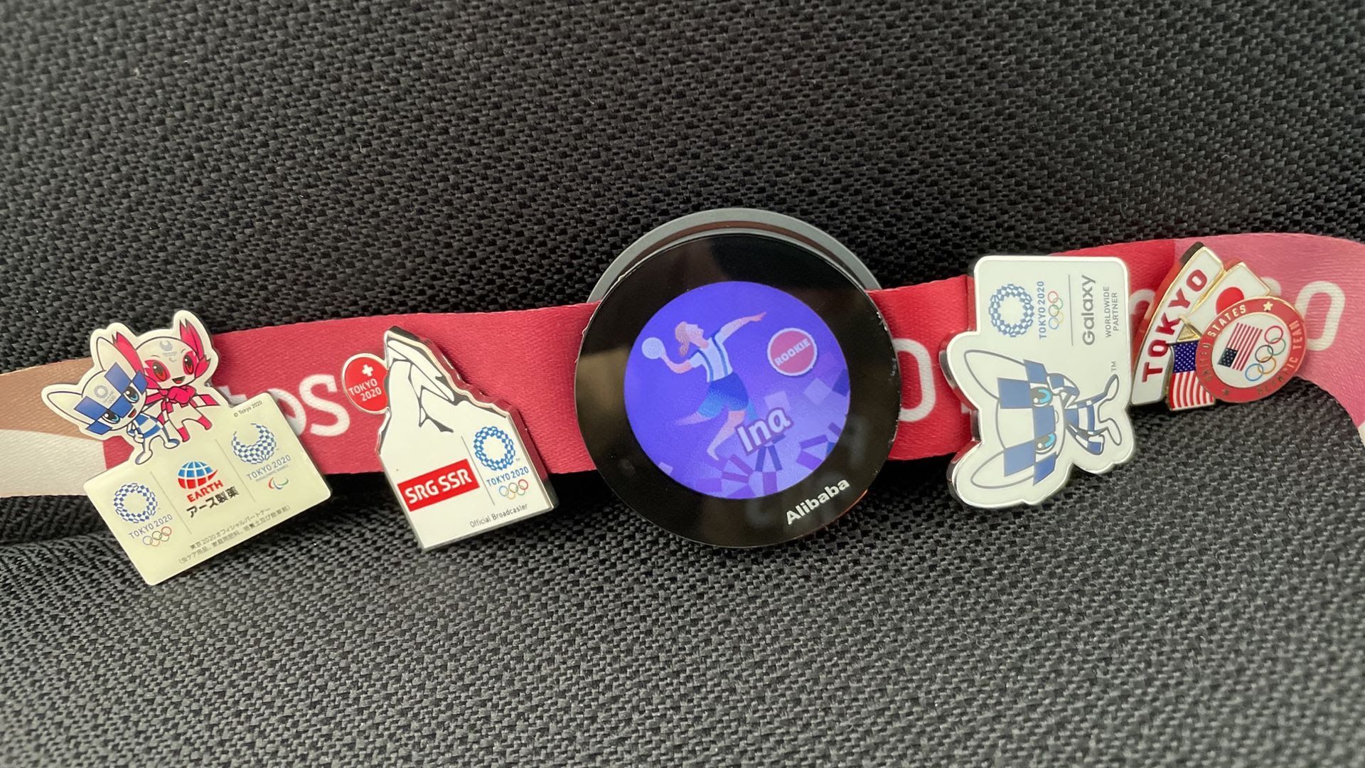 Photo of round-screen digital device next to traditional Olympic pins attached to a strap