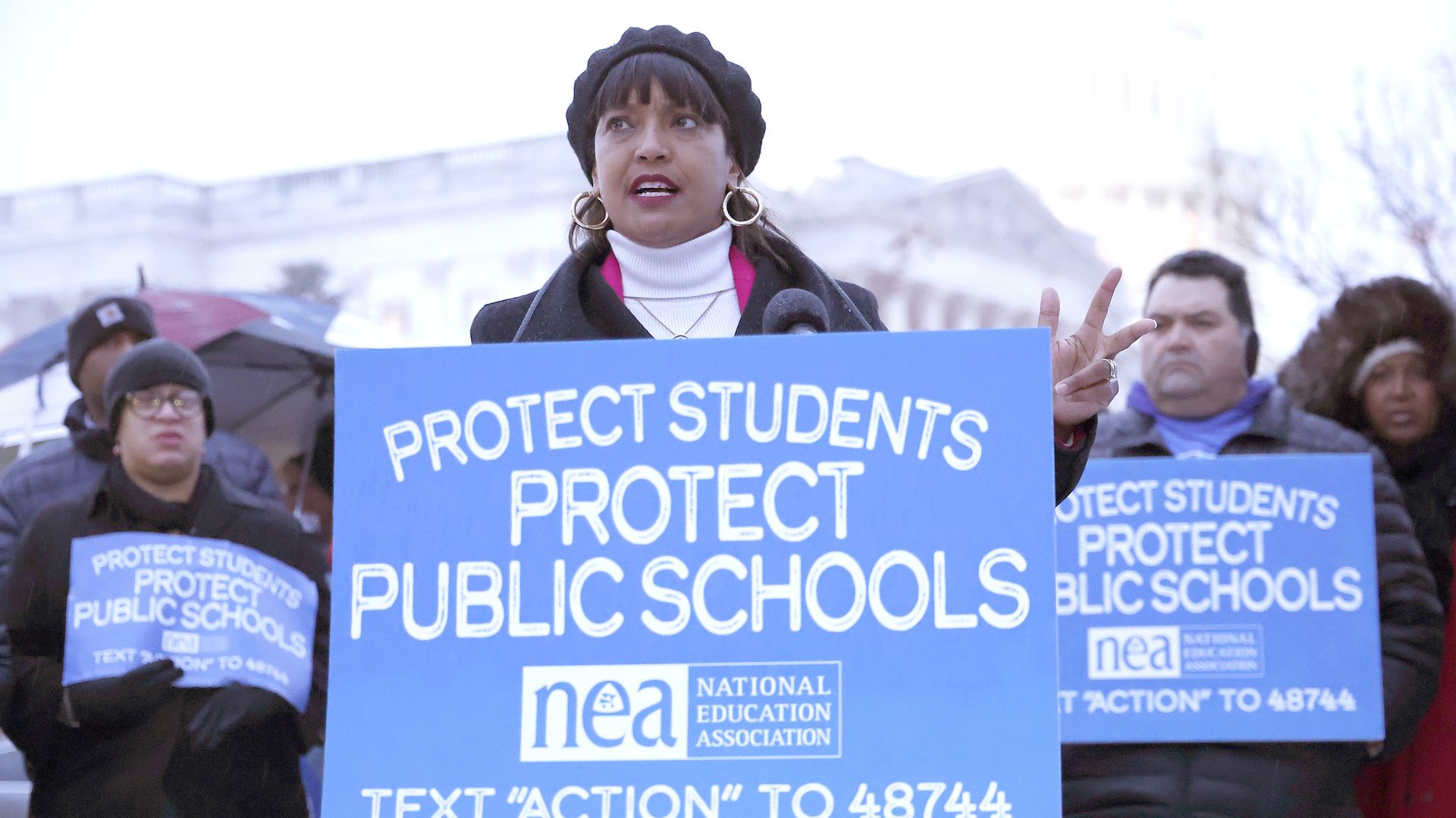 Rep. Jahana Hayes speaking in front of a crowd at a podium with a "PROTECT STUDENTS PROTECT PUBLIC SCHOOLS" sign from the National Education Association.