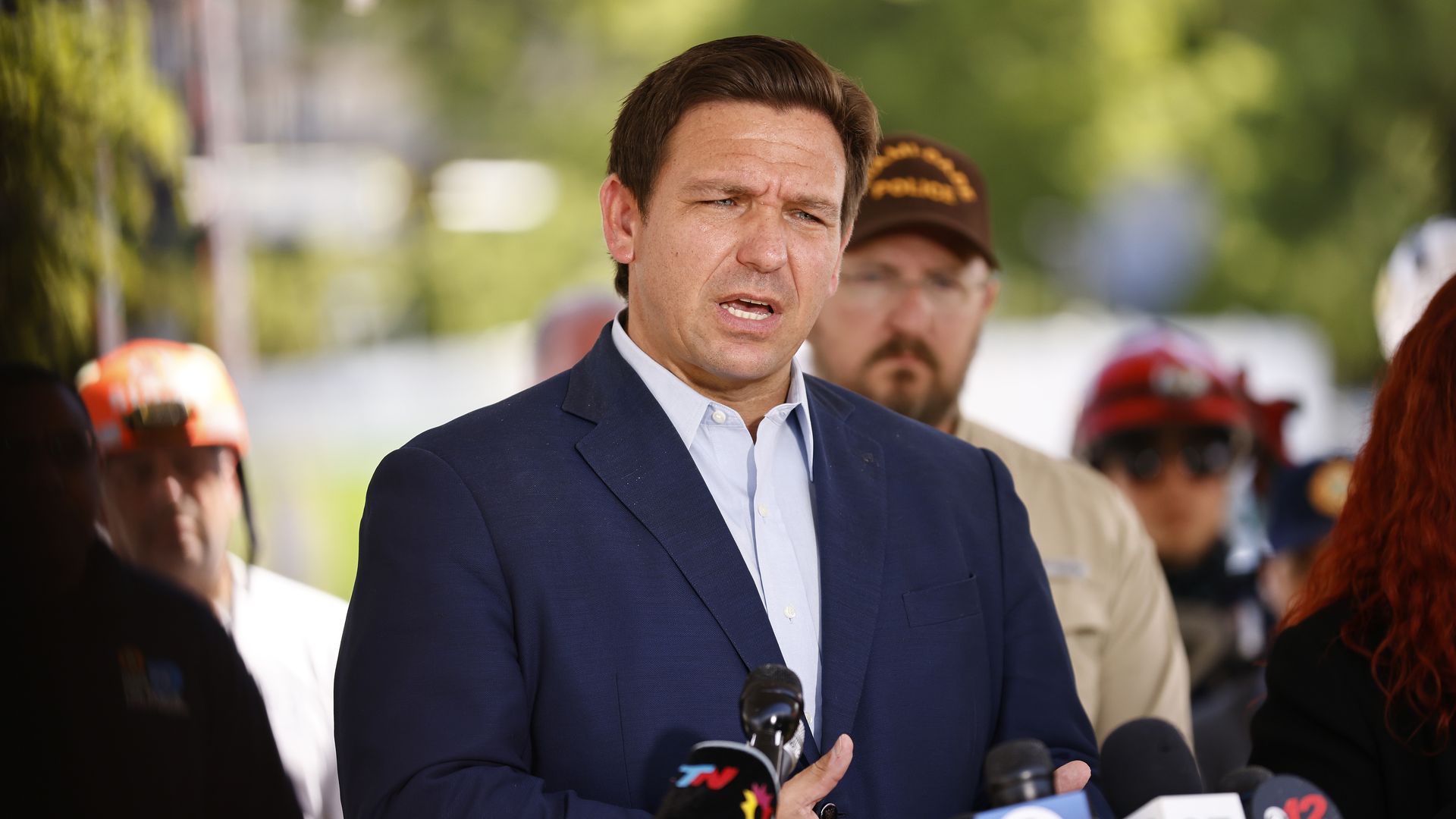Photo of Ron DeSantis speaking before a group of microphones at an outdoors conference