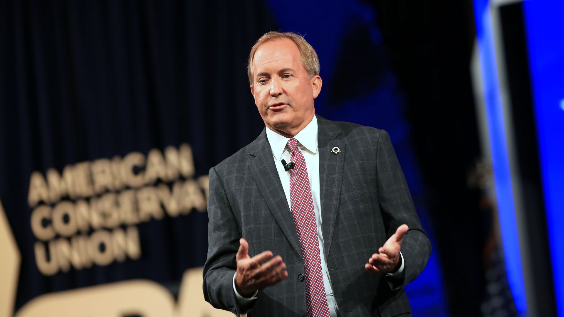 Photo of Ken Paxton speaking on a stage with both hands raised