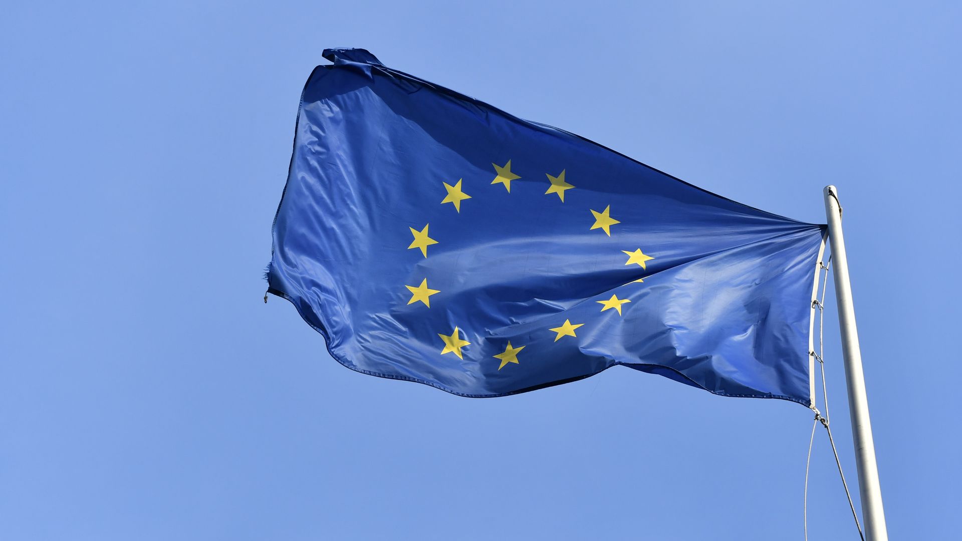 The blue and yellow flag of the European Union waves against the sky.