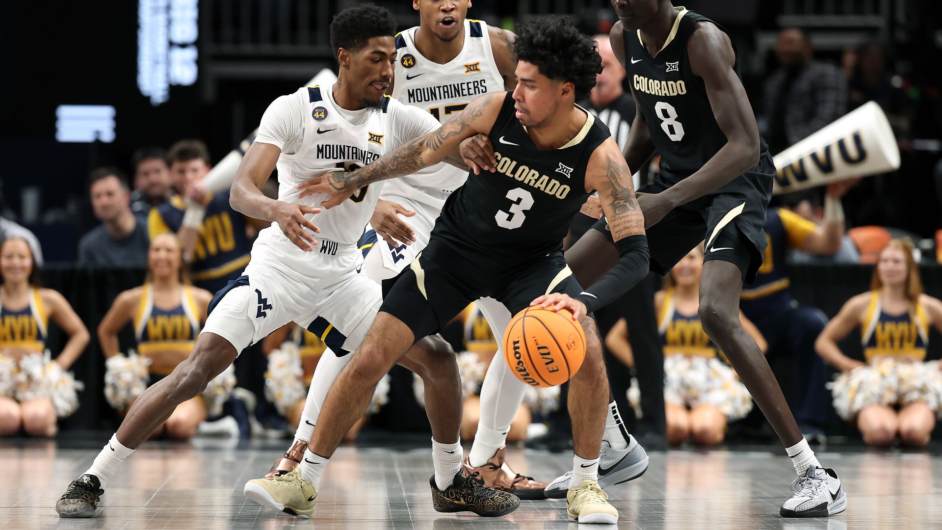 A man in a black jersey holds a basketball while attempting to keep another man from grabbing it. 