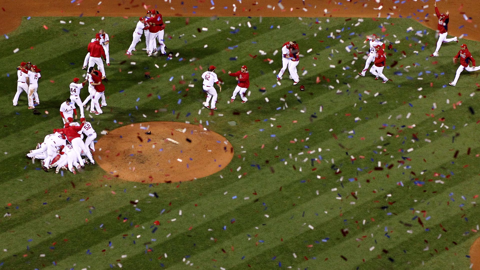 Cardinals players charge the field as confetti falls in front of the camera.