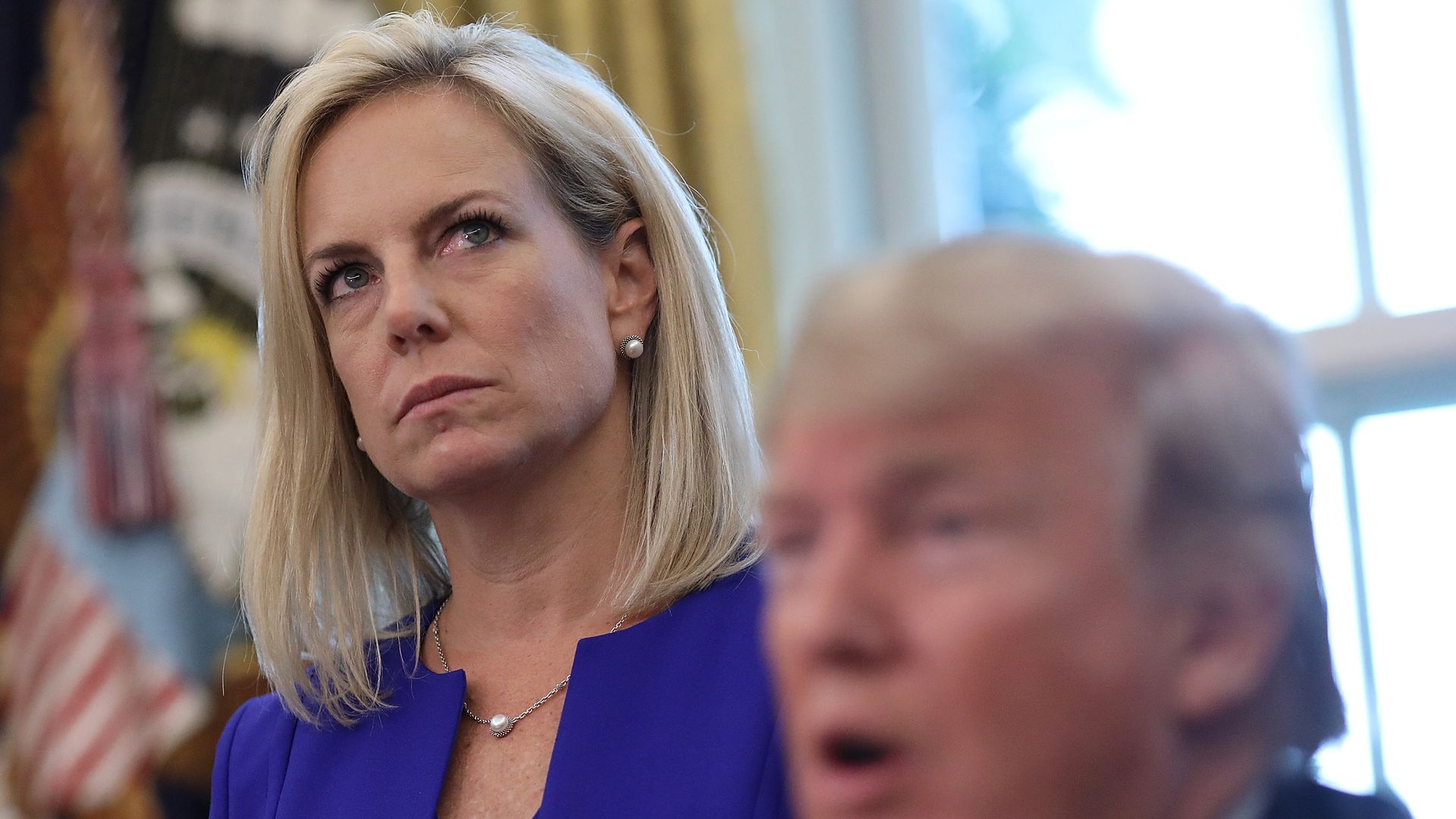 Secretary Nielsen, in focus and in purple looks sternly over Trump's head, who is not in focus
