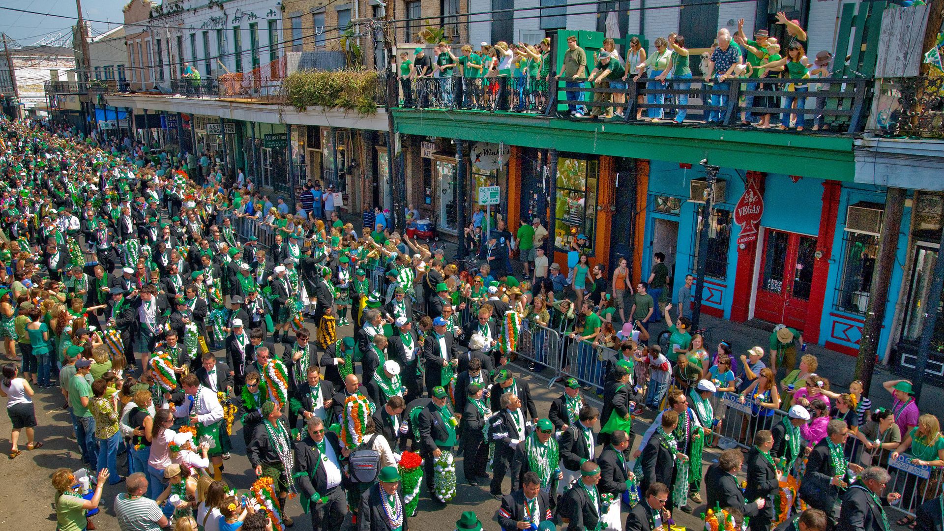 Hundreds of men clad in green march in a parade down Magazine Street in New Orleans as parade-goers watch from the street and balconies above the crowd.