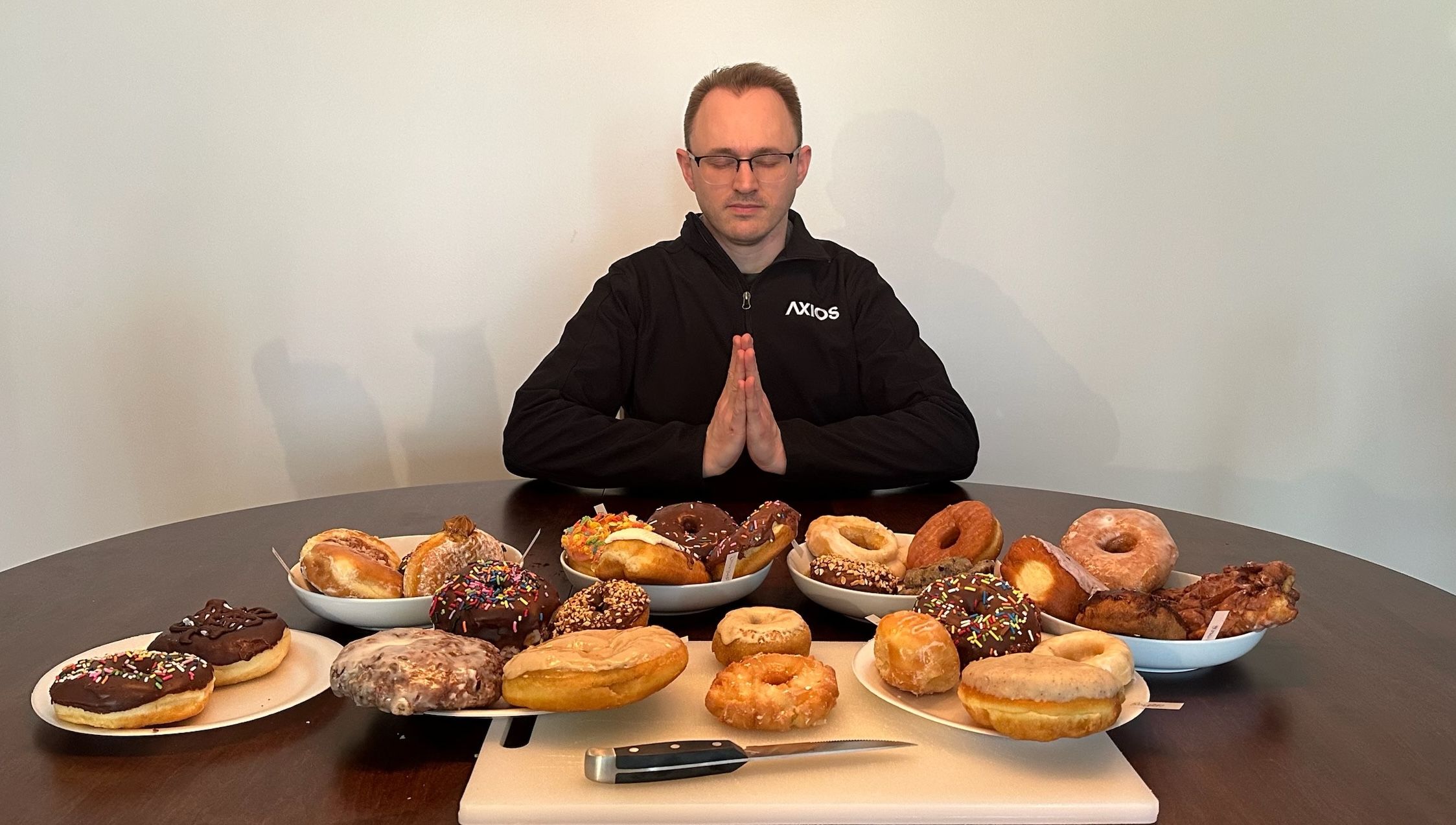 A strange man sits at a dining room table arrayed with donuts on plates