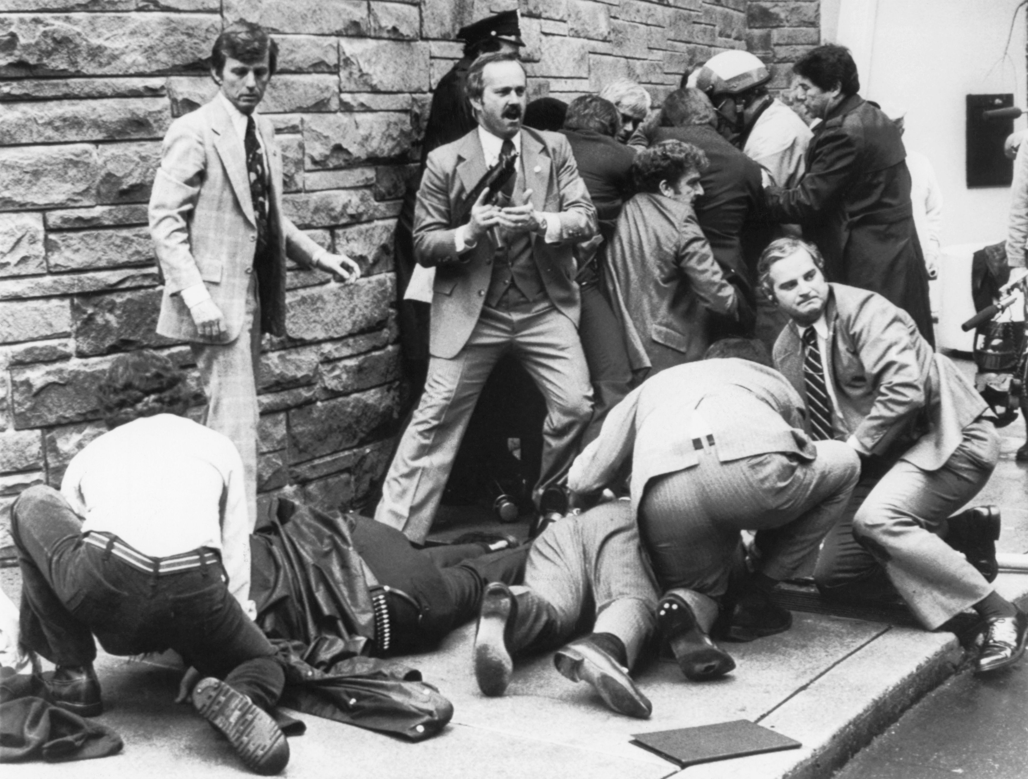 Photo of law enforcement surrounding two people who are laying on ground after a shooting 