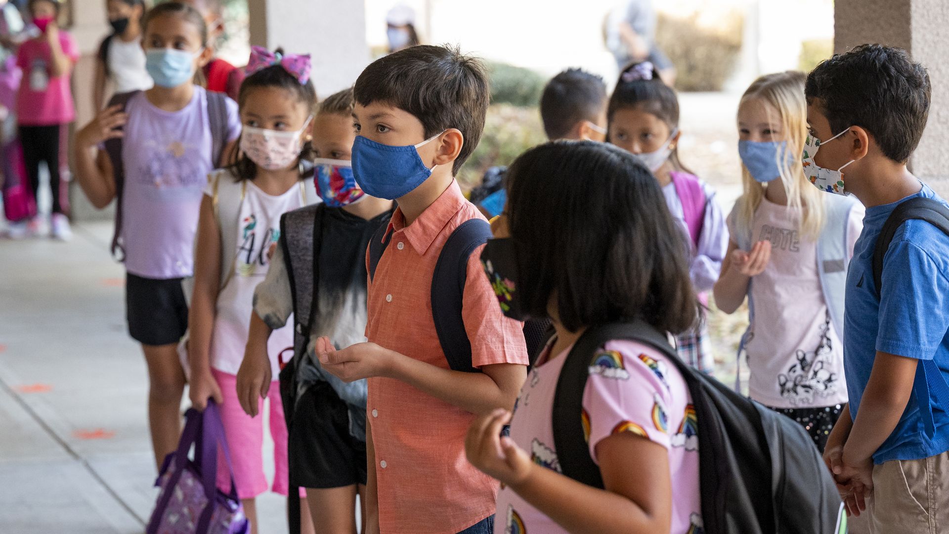 Students make their hand into a smile to show they are happy, since their mouths are covered, during the first day of class at Tustin Ranch Elementary School in Tustin, CA