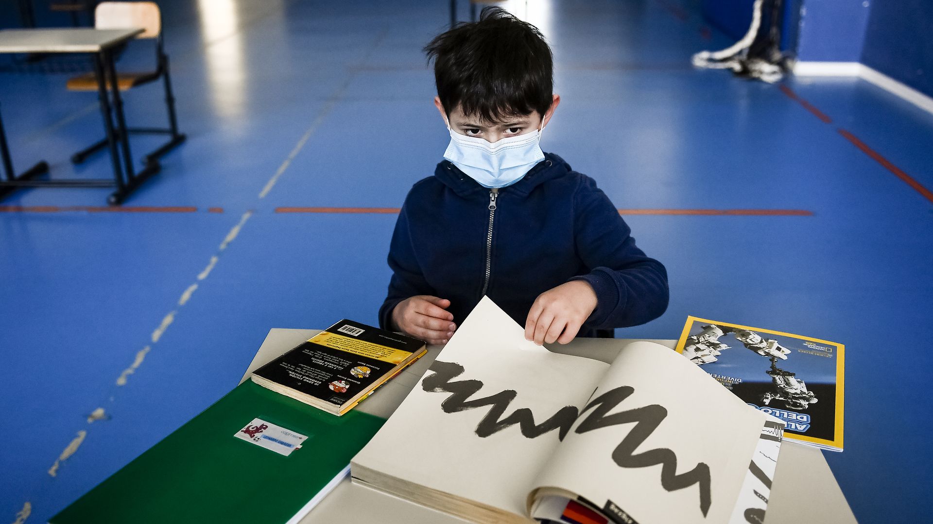 In this image, a young boy wears a face mask and flips through an art book