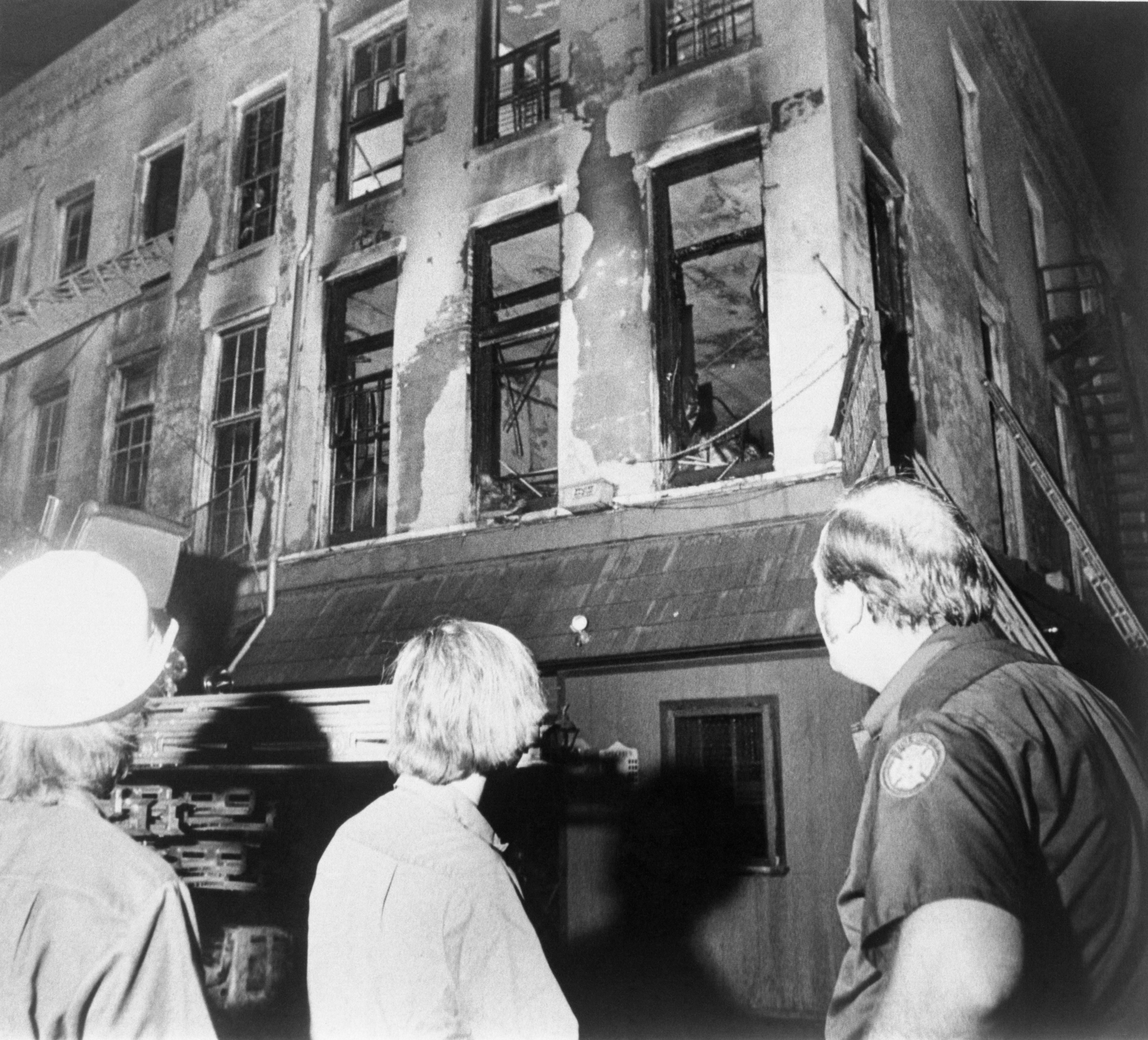 image shows a black and white photo of a burned building with three people looking at it.