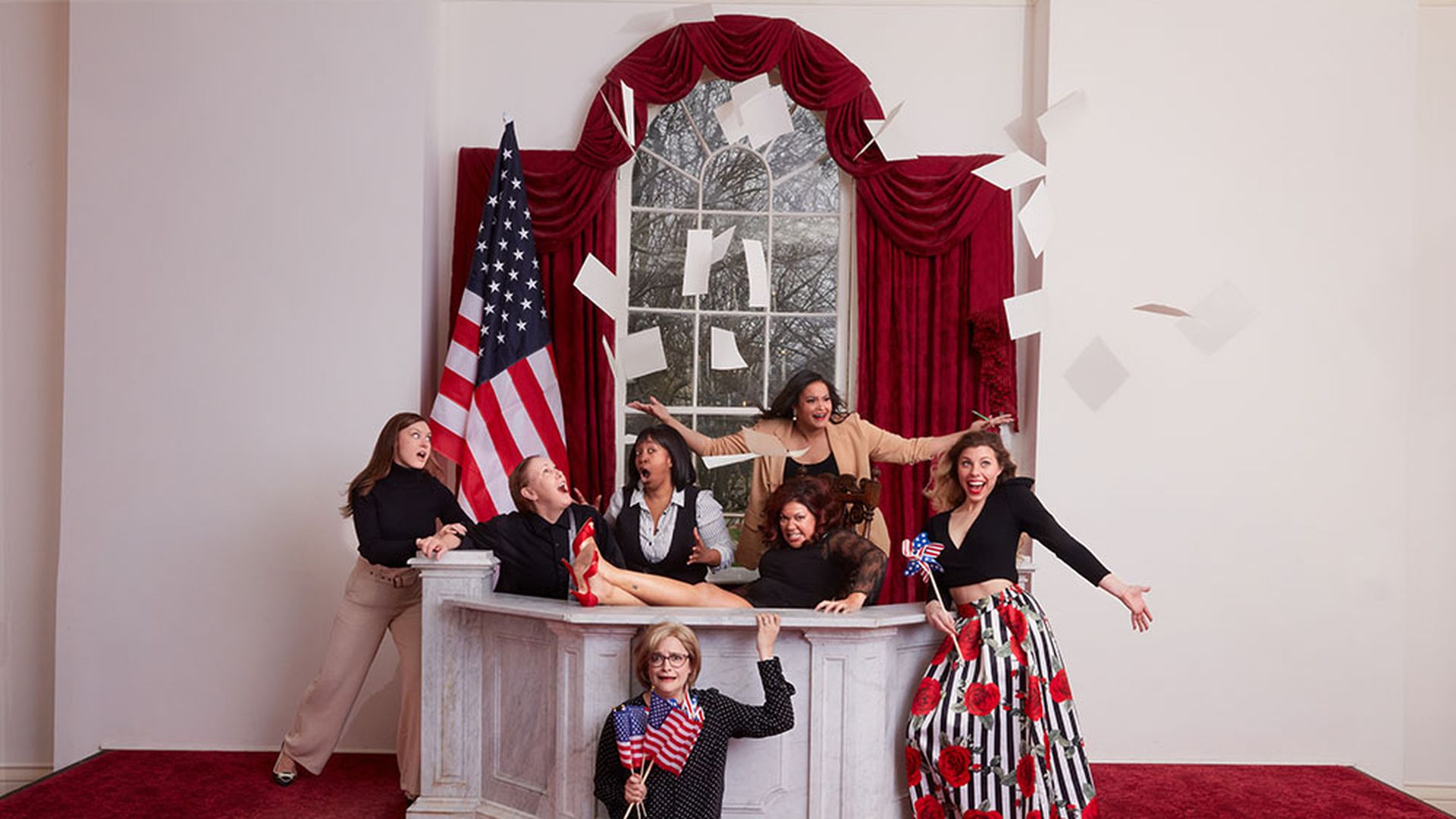 "POTUS" actors pose in a set of the Oval Office with paper flying in the air.