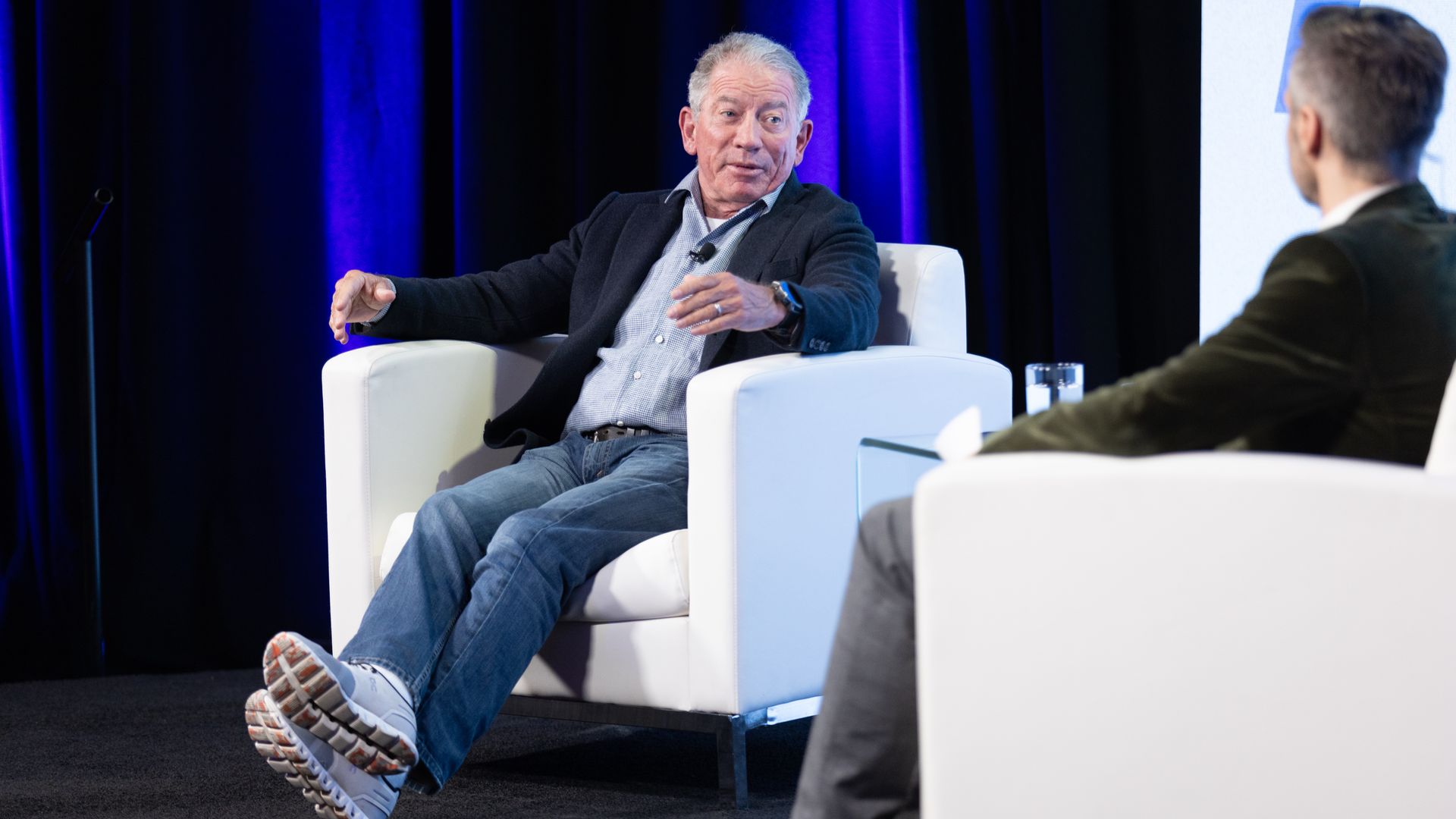 Two men sitting in chairs talking on a stage