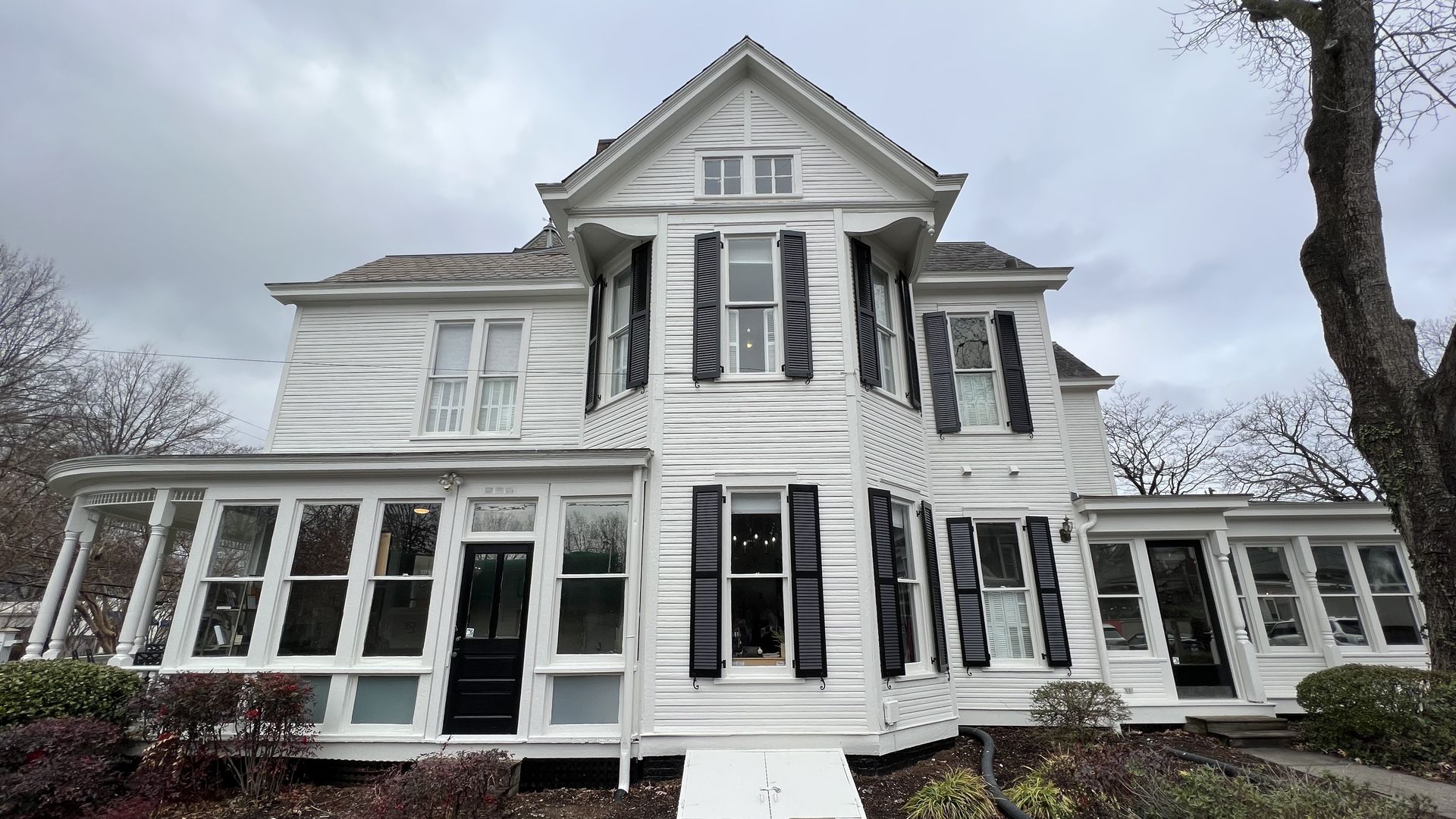 White three-story victorian home with a wrap around porch and black shutters.